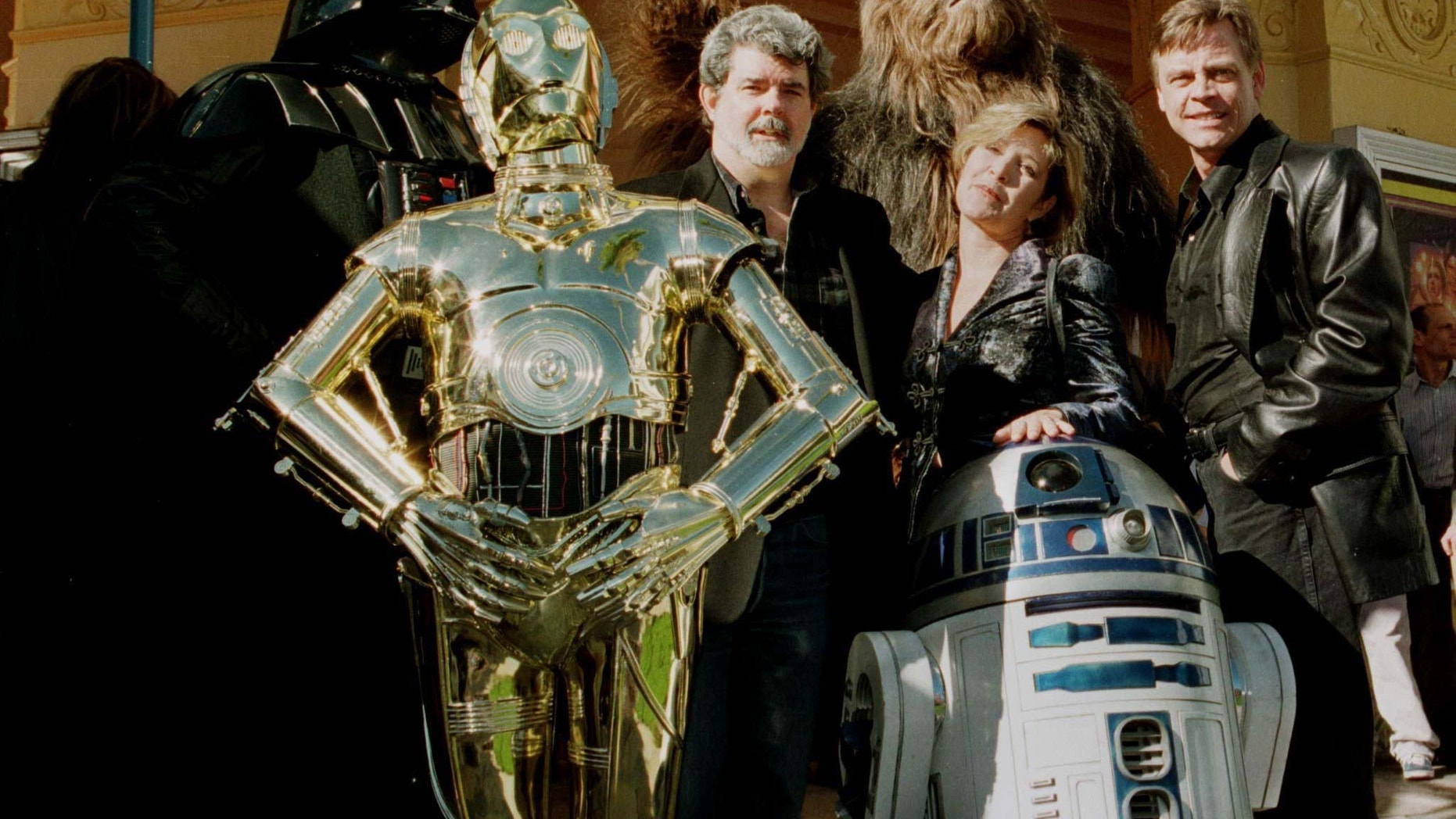 Director and writer of "Star Wars," George Lucas (C) poses with cast members Carrie Fisher and Mark Hamill along with characters "Darth Vader" (L) "3CPO" (in gold) "R2D2" (short robot) and "Chewbacca" (background) during the premiere of "Star Wars Special Editon" January 18, 1997 in Los Angeles.