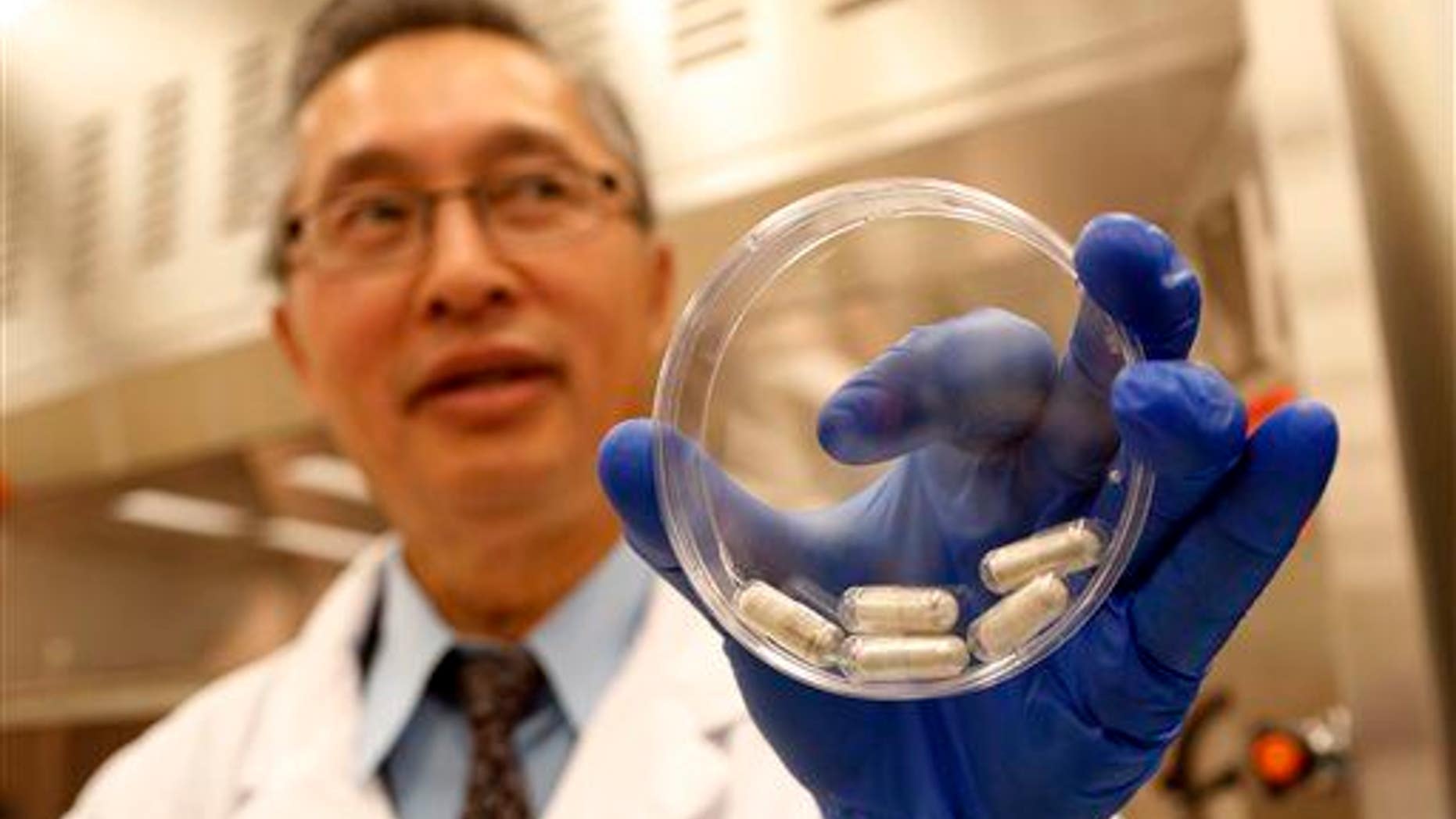 Dr. Thomas Louie, an infectious disease specialist, holds a container of stool pills in triple-coated gel capsules in his lab in Calgary, Alberta, Canada on Thursday, Sept. 26, 2013.