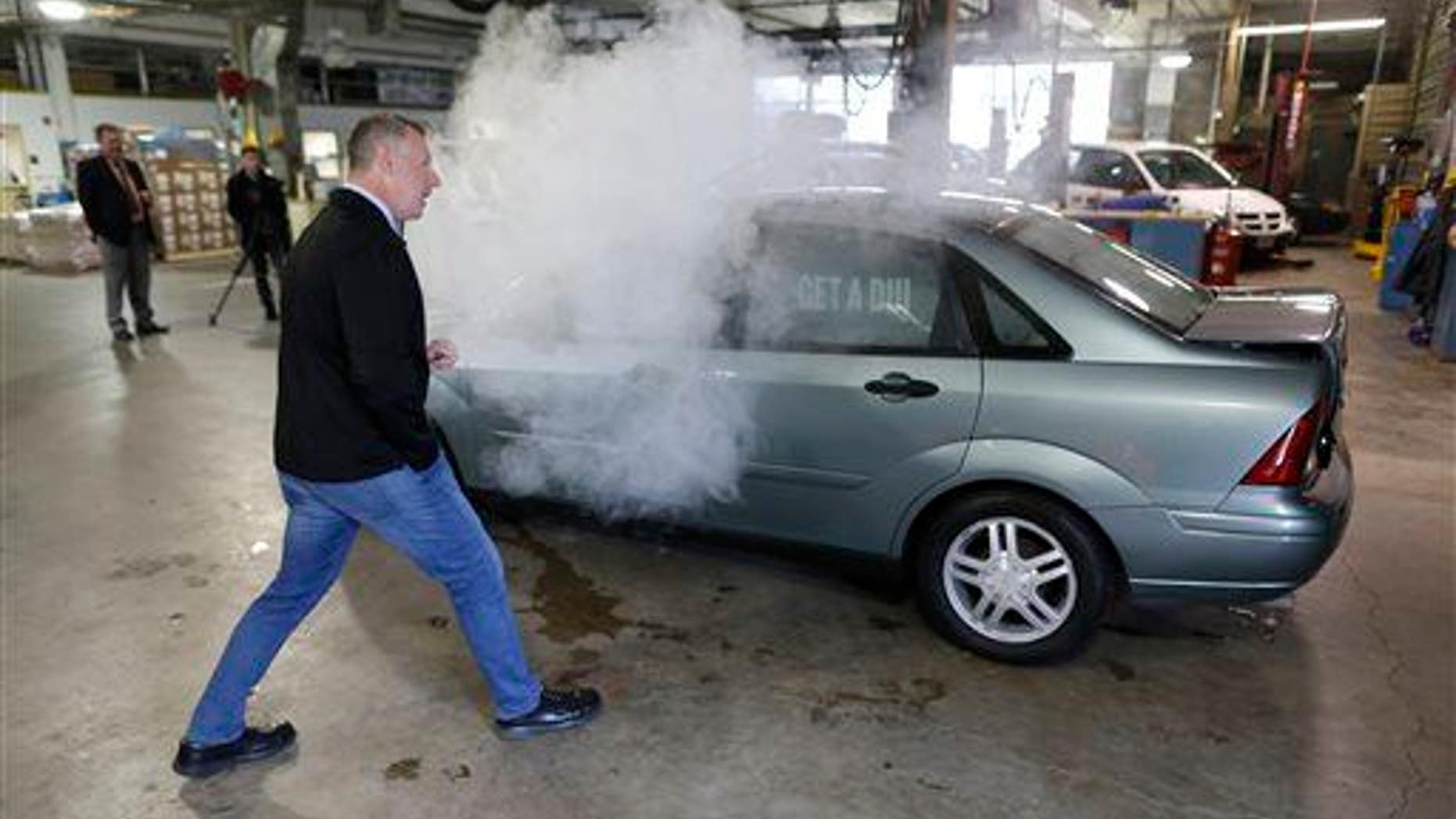 In this April 2015 photo, reporter Trevor Hughes gets a closer look as smoke billows out of car used in a campaign by the Colorado Department of Transportation to fight stoned driving.