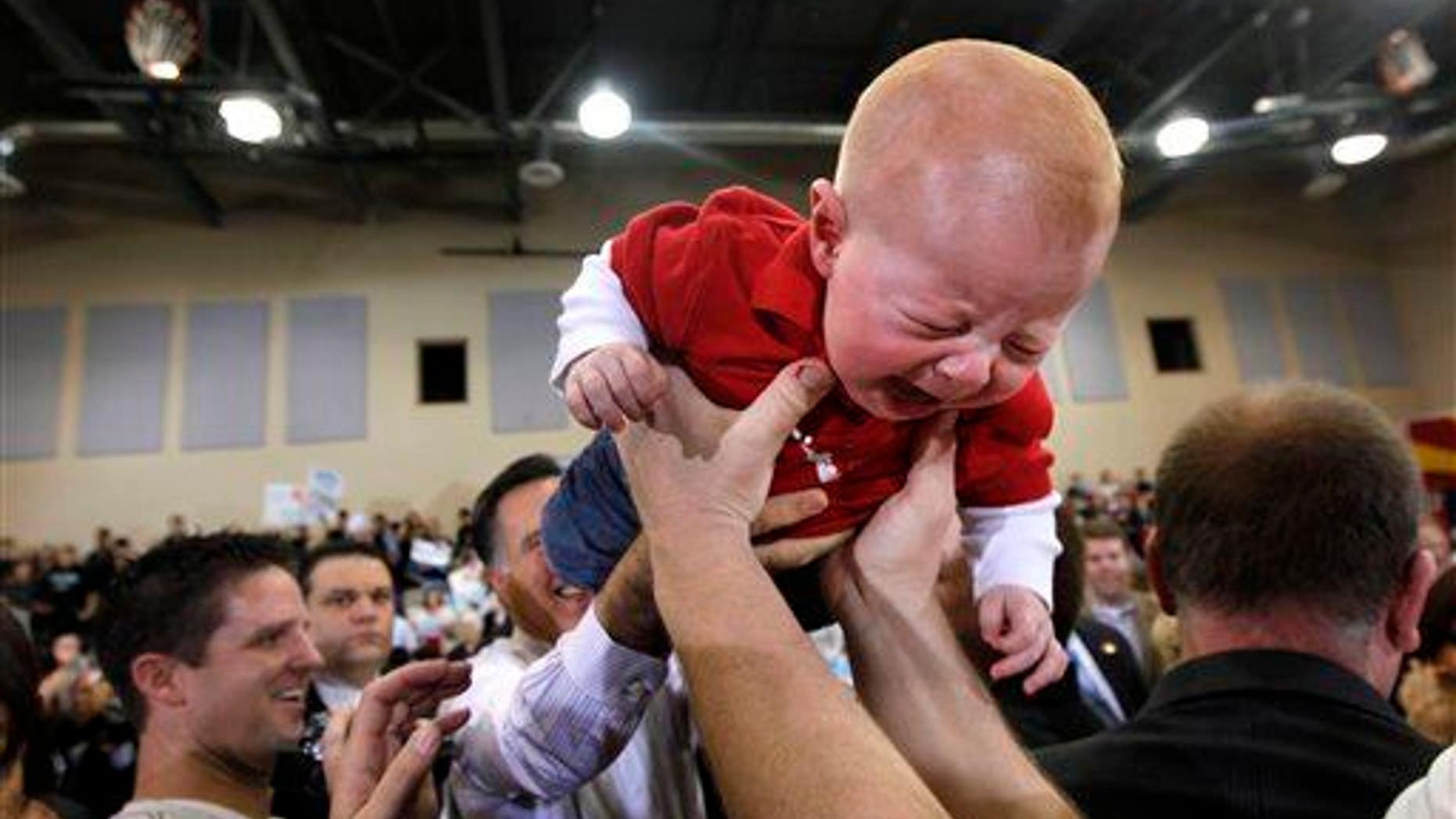 A baby cries as Republican presidential candidate, former Massachusetts Gov. Mitt Romney, background, returns it to the crowd after holding him up at a campaign rally at Tri-City Christian Academy in Chandler, Arizona, Wednesday, Feb. 22, 2012. (AP Photo/Gerald Herbert)