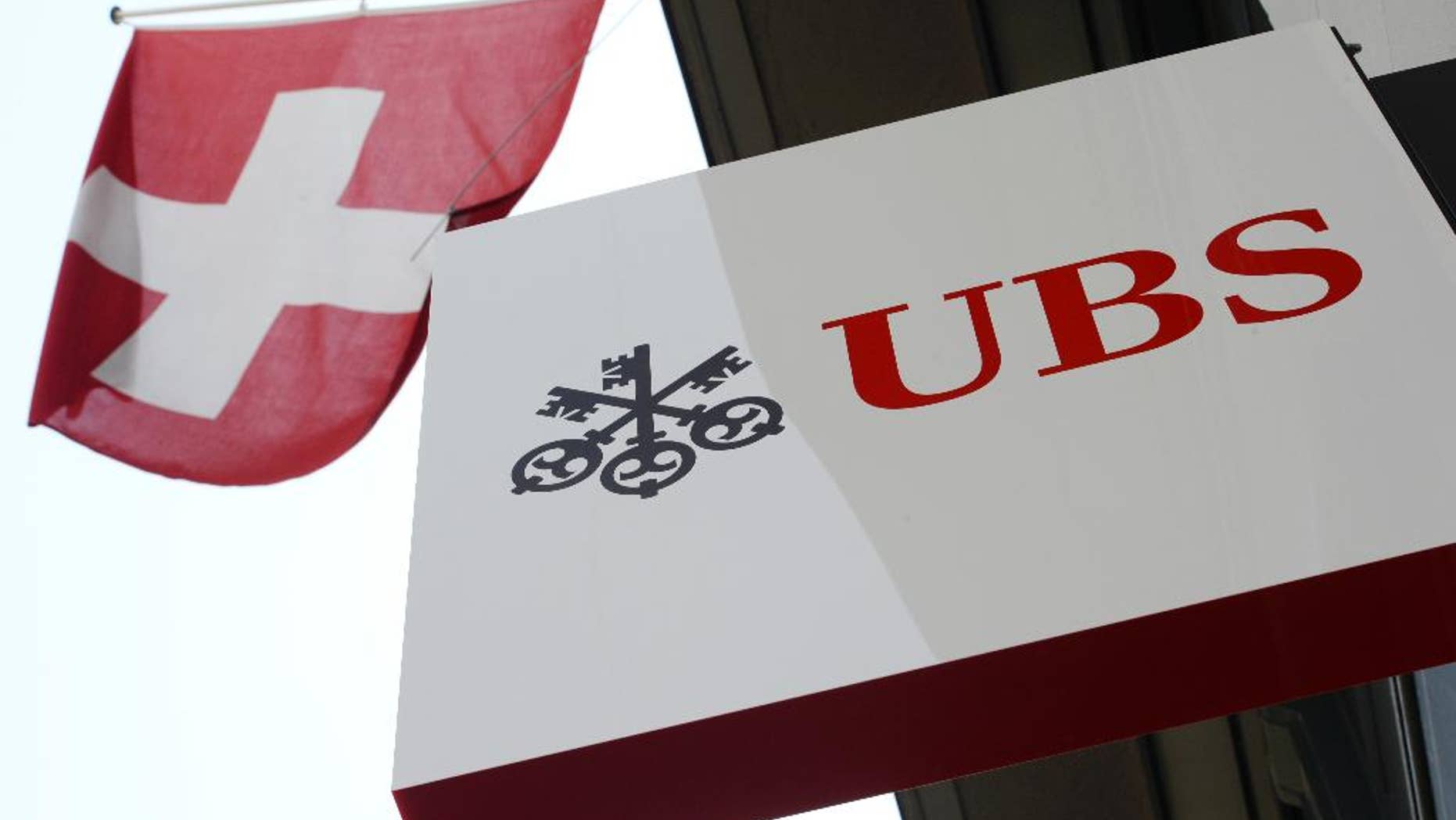 FILE - The April 24, 2014 file photo shows the logo of Swiss bank UBS and the Swiss flag in Zurich, Switzerland. UBS has reported a 71 percent increase in third quarter profit, Tuesday Nov. 3, 2015, as the banking giant took a big tax benefit, while predicting "substantial" future costs from new Swiss regulations aimed at bucking up the country's two biggest financial institutions. (Steffen Schmidt/Keystone via AP,File)