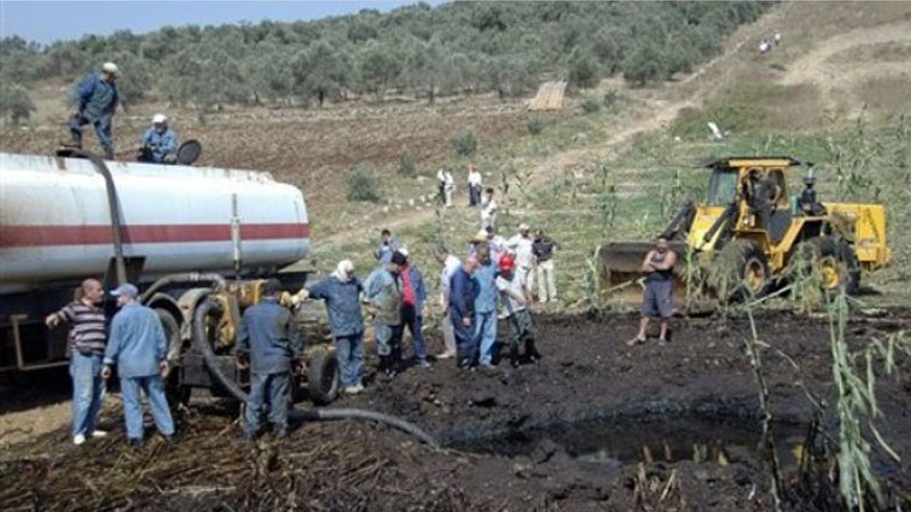 July 29, 2011: In this photo released by the Syrian official news agency SANA, workers pump oil from the site of a bomb blast that struck a major oil pipeline in the western town of Talkalakh, Syria.