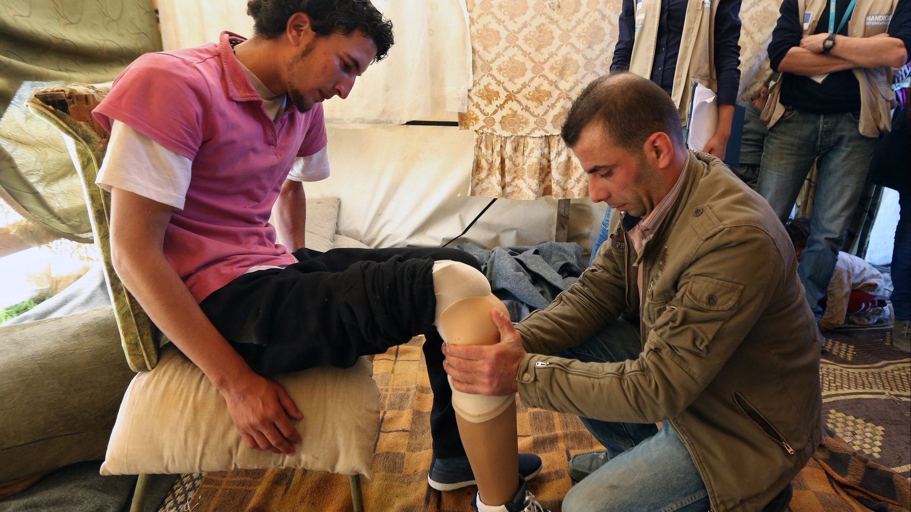 Mustafa Ahmad, left, a 19-year-old who lost his leg in his hometown of Deir Hafer in Aleppo province in November 2011 when government warplanes bombed his neighborhood, is fitted with a prosthetic leg by a Lebanese prosthetic limb maker, right, at the Syrian refugee camp in Jib Janine, in the Bekaa valley, Lebanon.