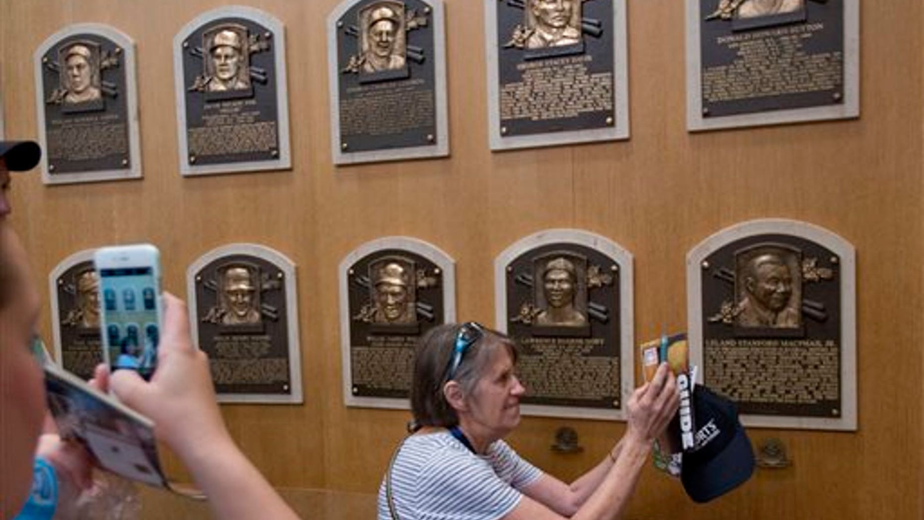Fans visit the Plaque Gallery at the National Baseball Hall of Fame on Saturday, July 25, 2015, in Cooperstown, N.Y. Former Major League Baseball players Pedro Martinez, Randy Johnson, Craig Biggio and John Smoltz will be inducted to the hall on Sunday. (AP Photo/Mike Groll)