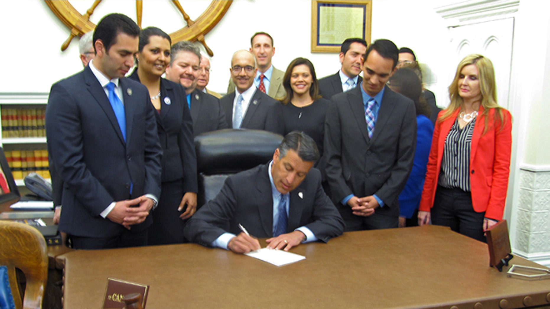 Nevada Gov. Brian Sandoval signs a bill, AB27, into law at the capitol in Carson City as lawmakers look on. The measure would allow immigrants with temporary legal status to get a Nevada teacher's license. (AP Photo/Michelle Rindels)