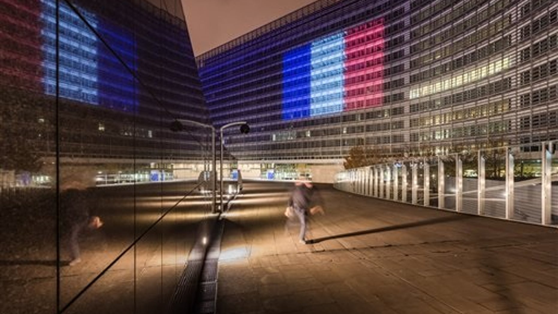A man walks by the EU Commission headquarters illuminated with the colors of the French national flag in solidarity with France after the terror attacks in Paris, in Brussels on Sunday, Nov. 15, 2015. (AP Photo/Geert Vanden Wijngaert)