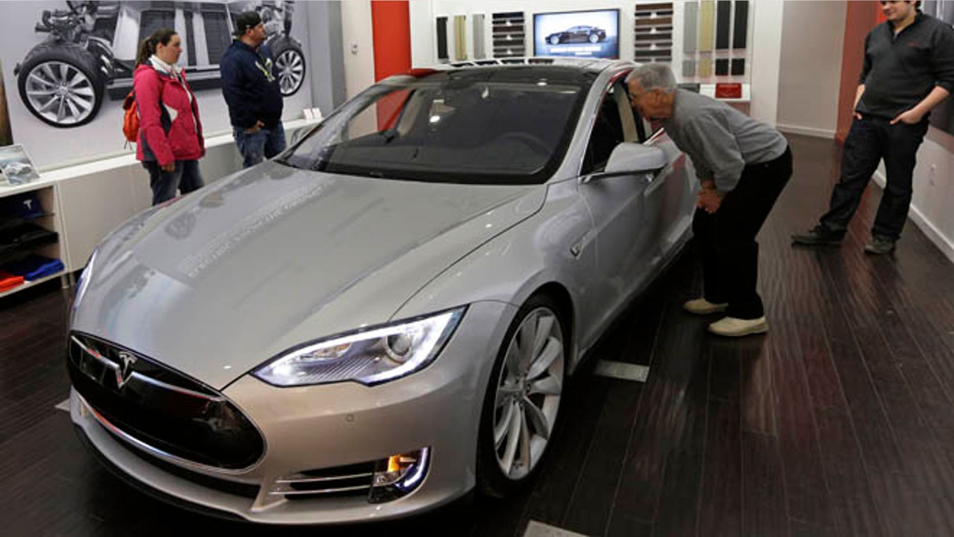 Tesla representative John Van Cleave, right, shows customers Sarah and Robert Reynolds, left, and Vince Giardina, a new Tesla all electric car, Monday, March 17, 2014, at a Tesla showroom inside the Kenwood Towne Centre in Cincinnati. Ohio auto dealers are sparring at the Statehouse with the California-based Tesla, which is selling it's next generation electric cars from three Ohio storefronts. Lawmakers in Ohio and other states are trying to block Tesla direct sales on grounds they undercut traditional auto dealerships. (AP Photo/Al Behrman)