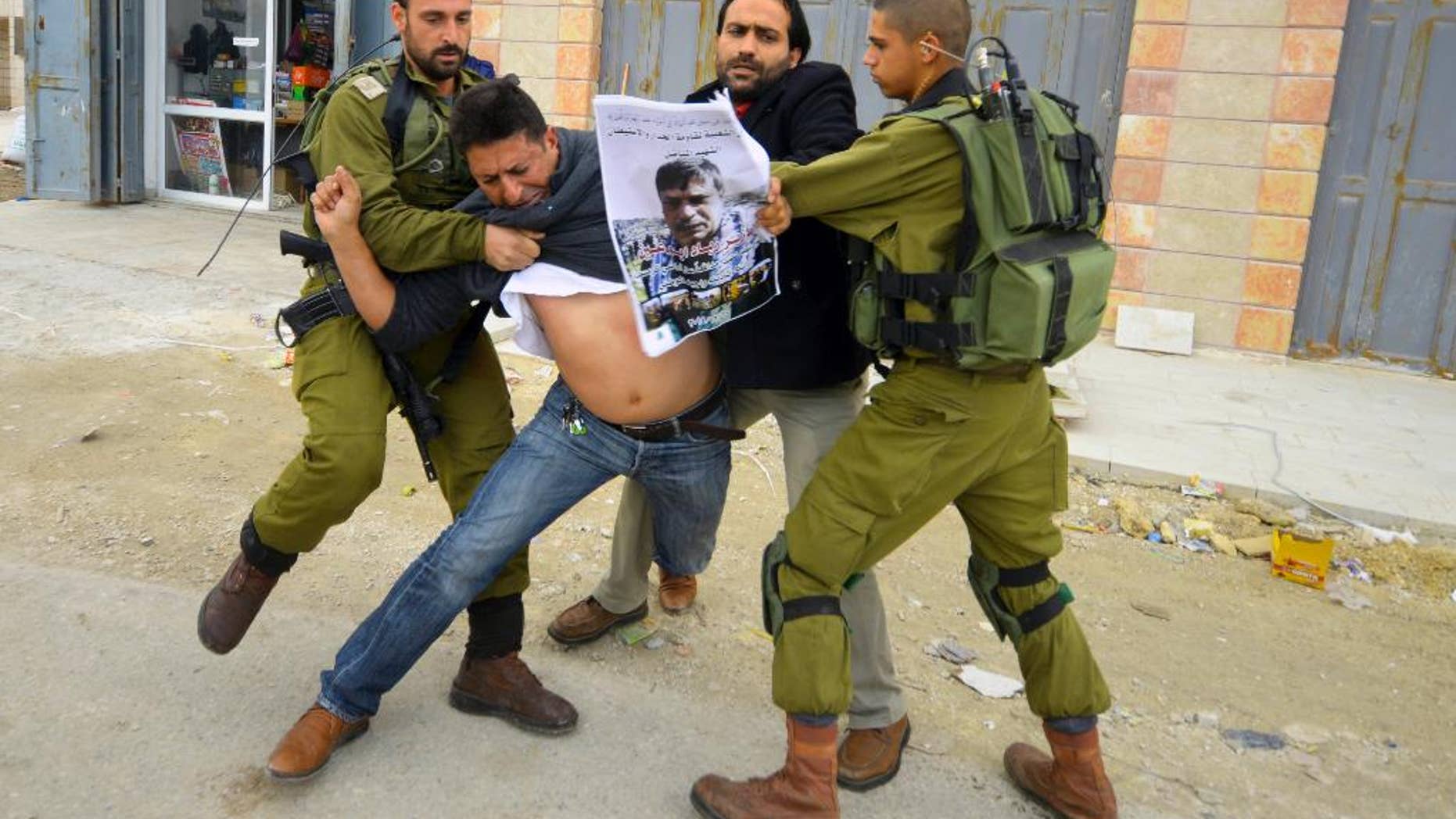 In this Friday, Dec. 12, 2014 photo, Israeli soldiers grab a Palestinian holding a poster showing late Cabinet minister Ziad Abu Ain during a protest in Bethlehem, West Bank. Abu Ain collapsed and died shortly after scuffling with Israeli troops during a West Bank protest Wednesday. (AP Photo/Mahmoud Illean)