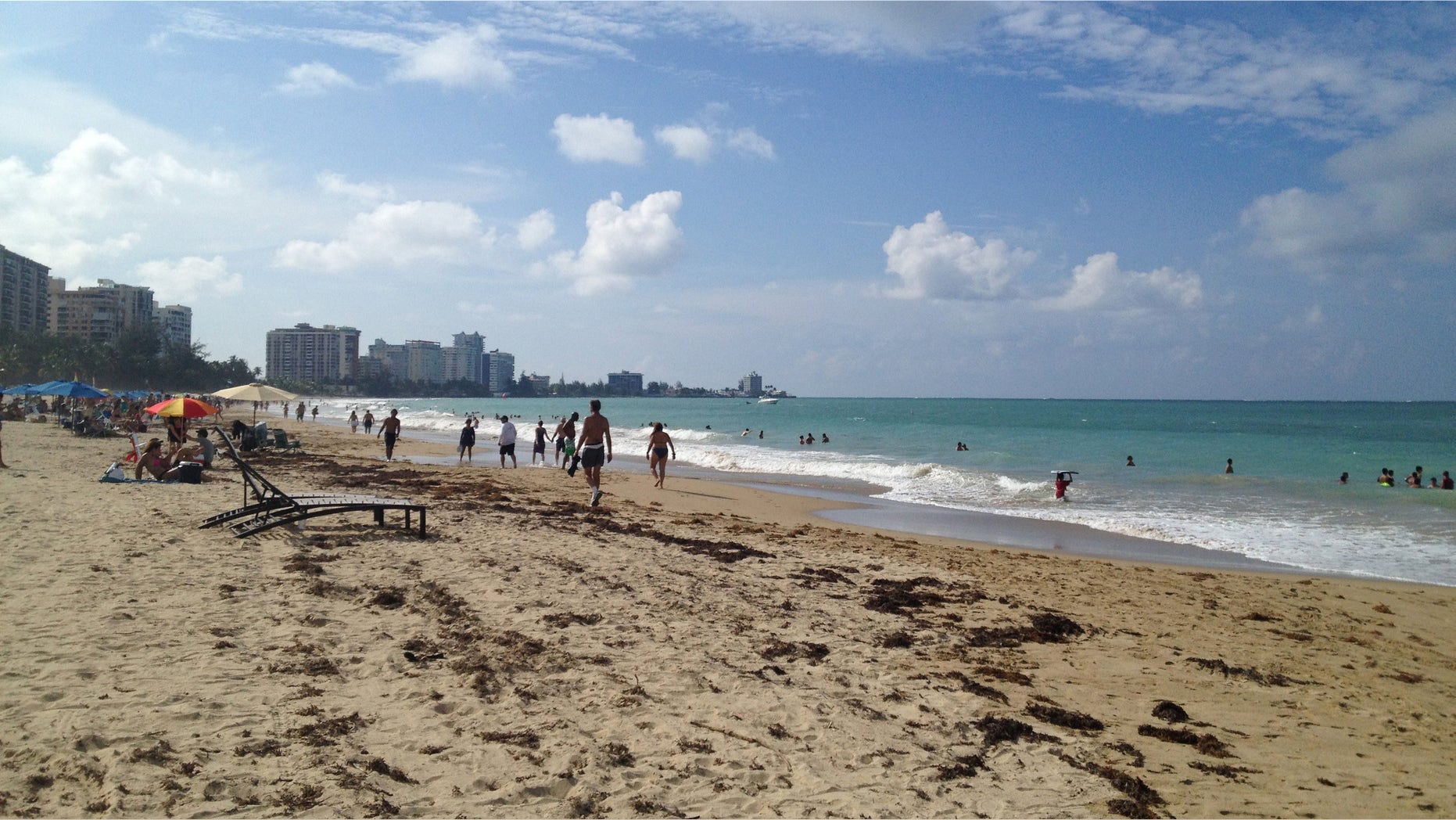 In this Oct. 2014 photo, beachgoers enjoy the sun and sand at Isla Verde Beach in San Juan, Puerto Rico. Puerto Rico, a U.S. territory, offers all the comforts of domestic travel - easy entry, no extra charges for cell phone service, and the U.S. dollar as the currency - along with Caribbean beaches and Latin culture, waterfalls, colonial Spanish history and good food and drink. (AP Photo/Kristi Eaton)