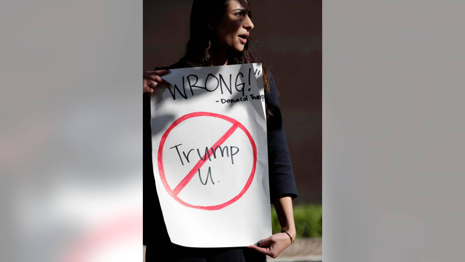 Senya Merchant holds a sign against President-elect Donald Trump's now-defunct Trump University Friday, Nov. 18, 2016, in San Diego. Trump agreed Friday to pay $25 million to settle several lawsuits alleging that his former school for real estate investors defrauded students who paid up to $35,000 to enroll in Trump University programs.(AP Photo/Gregory Bull)