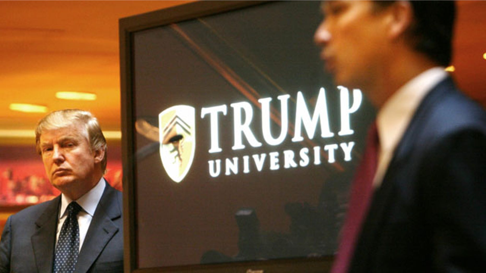 FILE- In this May 23, 2005 file photo, real estate mogul and Reality TV star August 25, 2013: Donald Trump, left, listens as Michael Sexton introduces him at a news conference in New York where he announced the establishment of Trump University. New York Attorney General Eric Schneiderman is suing Trump for $40 million, saying that “Trump University” didn’t deliver on its advertised promise to make students rich, but instead steered them into expensive yet mostly useless seminars. (AP Photo)