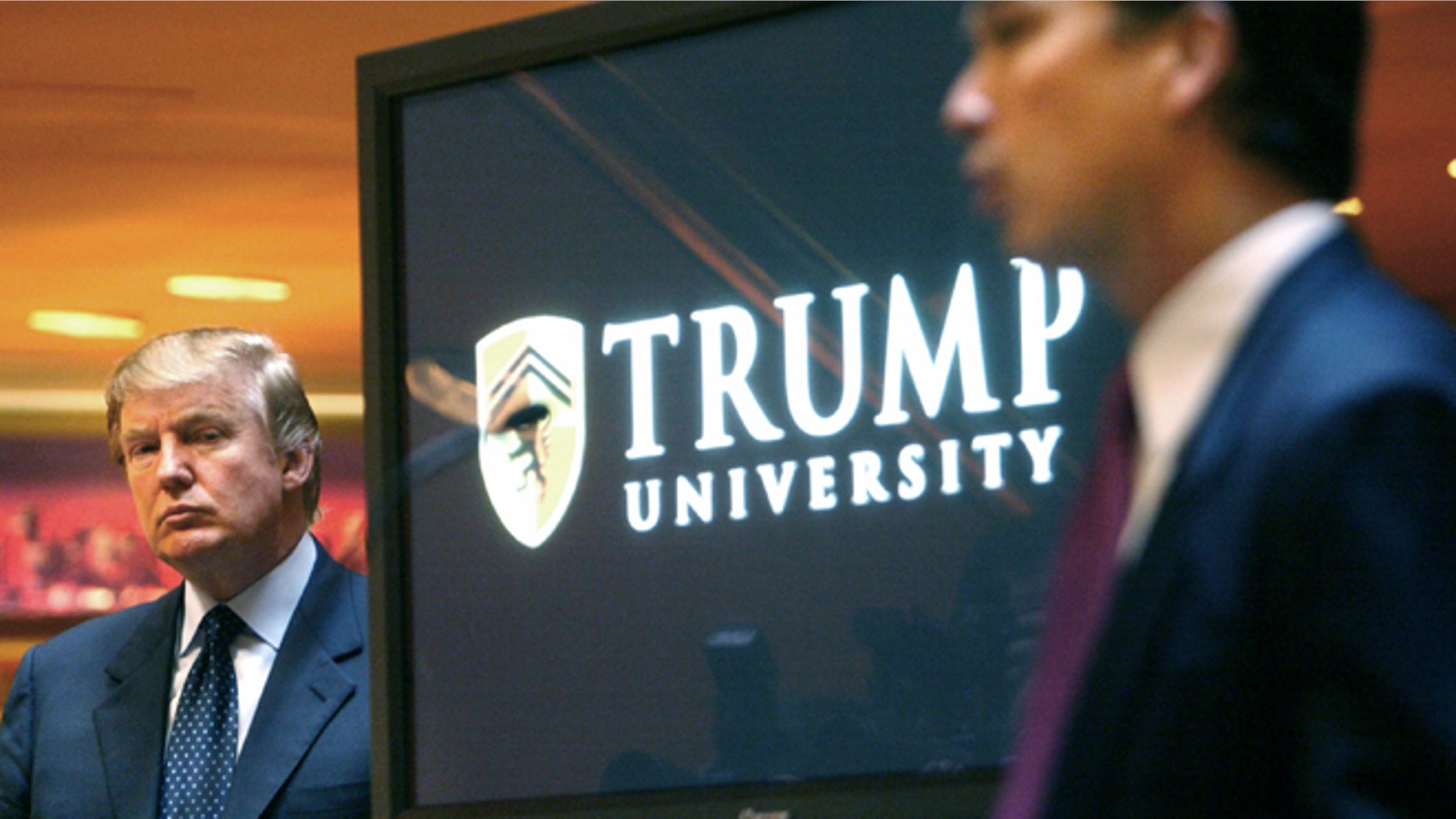 FILE- In this May 23, 2005 file photo, real estate mogul and Reality TV star Donald Trump, left, listens as Michael Sexton introduces him at a news conference in New York where he announced the establishment of Trump University. A federal judge who has been a target of Donald Trumps unending scorn must decide whether to release videos of the presumed Republican presidential nominee testifying in a lawsuit about the now-defunct Trump University, images that Trumps attorneys worry will be used to tarnish the campaign. (AP Photo/Bebeto Matthews, File)