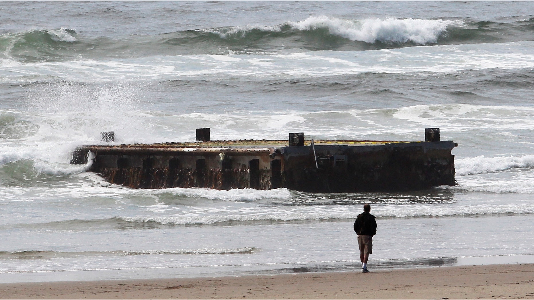 June 6, 2012: In this file photo, a man looks at a 70-foot-long dock with Japanese lettering that washed ashore on Agate Beach in Newport, Ore.