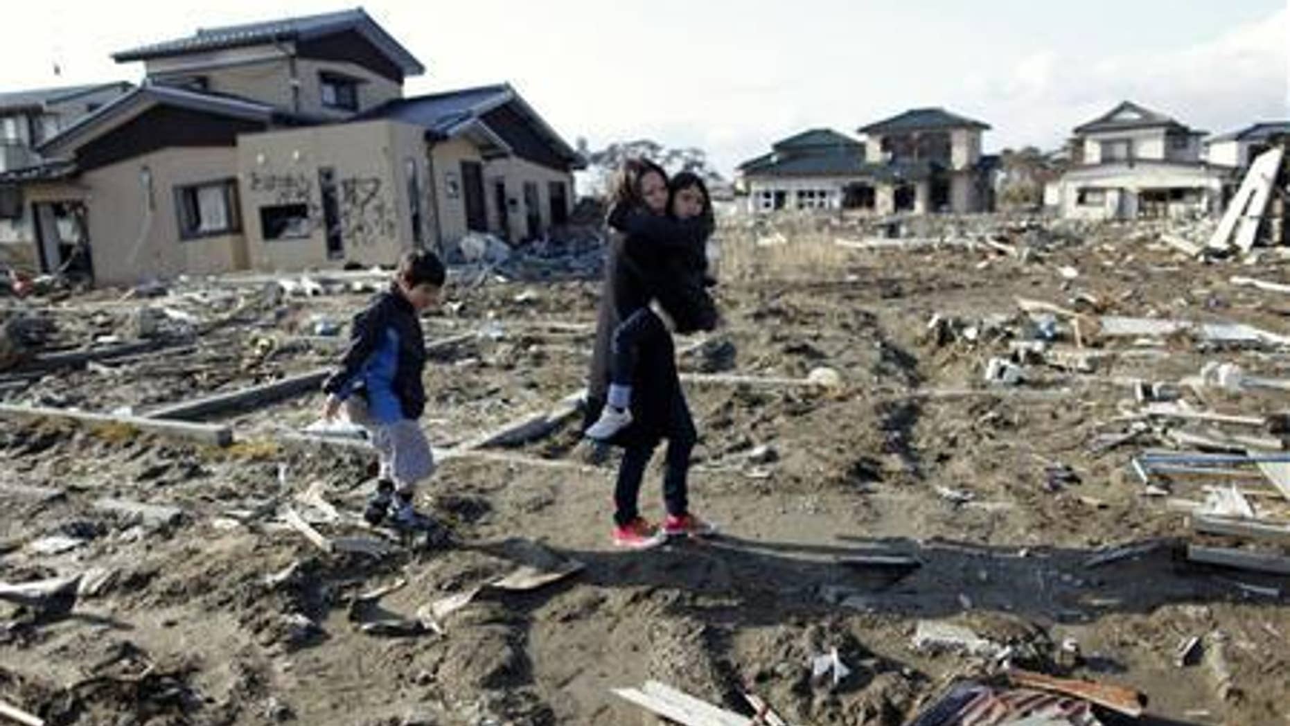 Wakana Kumagai, 7, carried by her mother Yoshiko and followed by her brother Koki visit the spot where their house, which was washed away by the March 11, 2011 tsunami, used to stand in Higashimatsushima, Miyagi prefecture