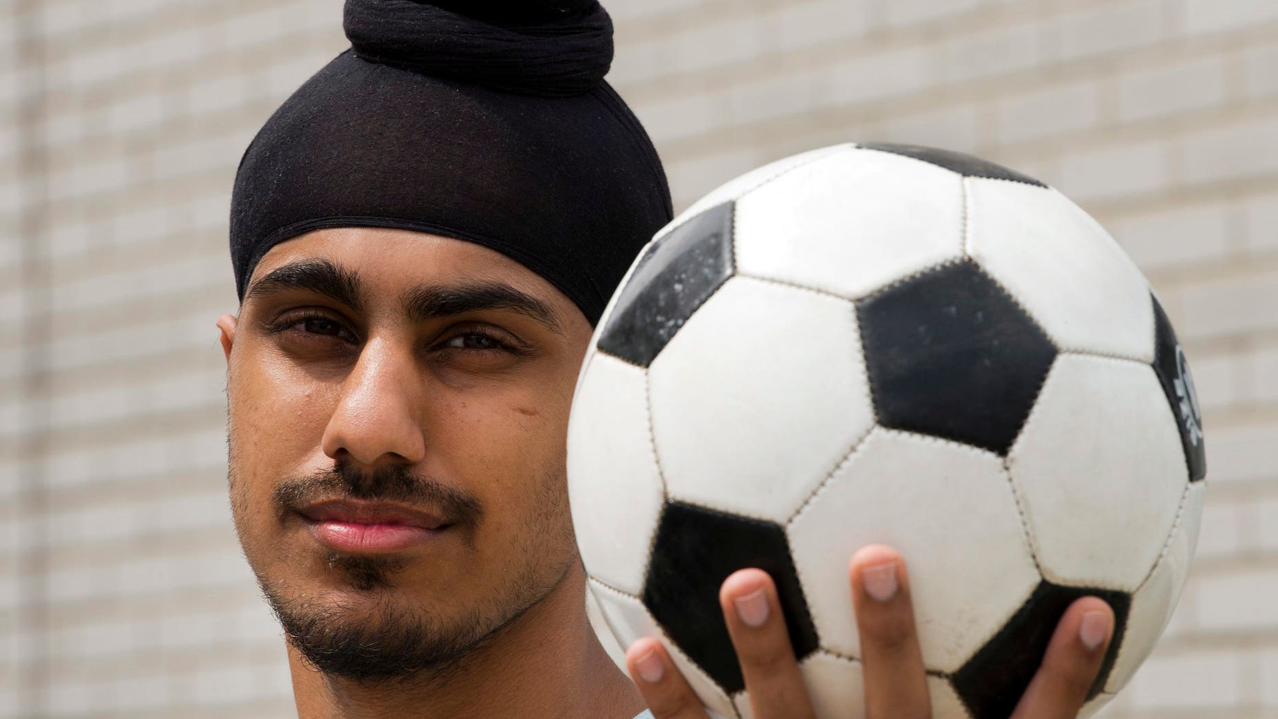 In this photo taken Wednesday, June 5, 2013, Aneel Samra, 18, holds a soccer ball in his backyard as he poses for a photo in Montreal. Samra said he's perplexed by the Quebec Soccer Federation's decision to uphold a year-old ban on Sikh turbans, patkas and keskis, without any evidence they pose a safety risk. (AP Photo/The Canadian Press, Ryan Remiorz)
