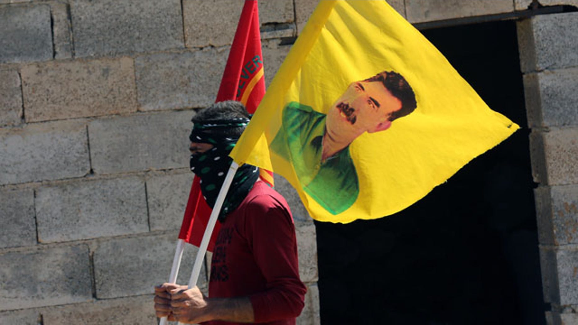 September 21, 2014: A masked protester waves a poster of jailed Kurdish rebel leader Abdullah Ocalan, amid a clash with security forces while several hundred Syrian refugees waited at the border in Suruc, Turkey. (AP Photo/Burhan Ozbilici)