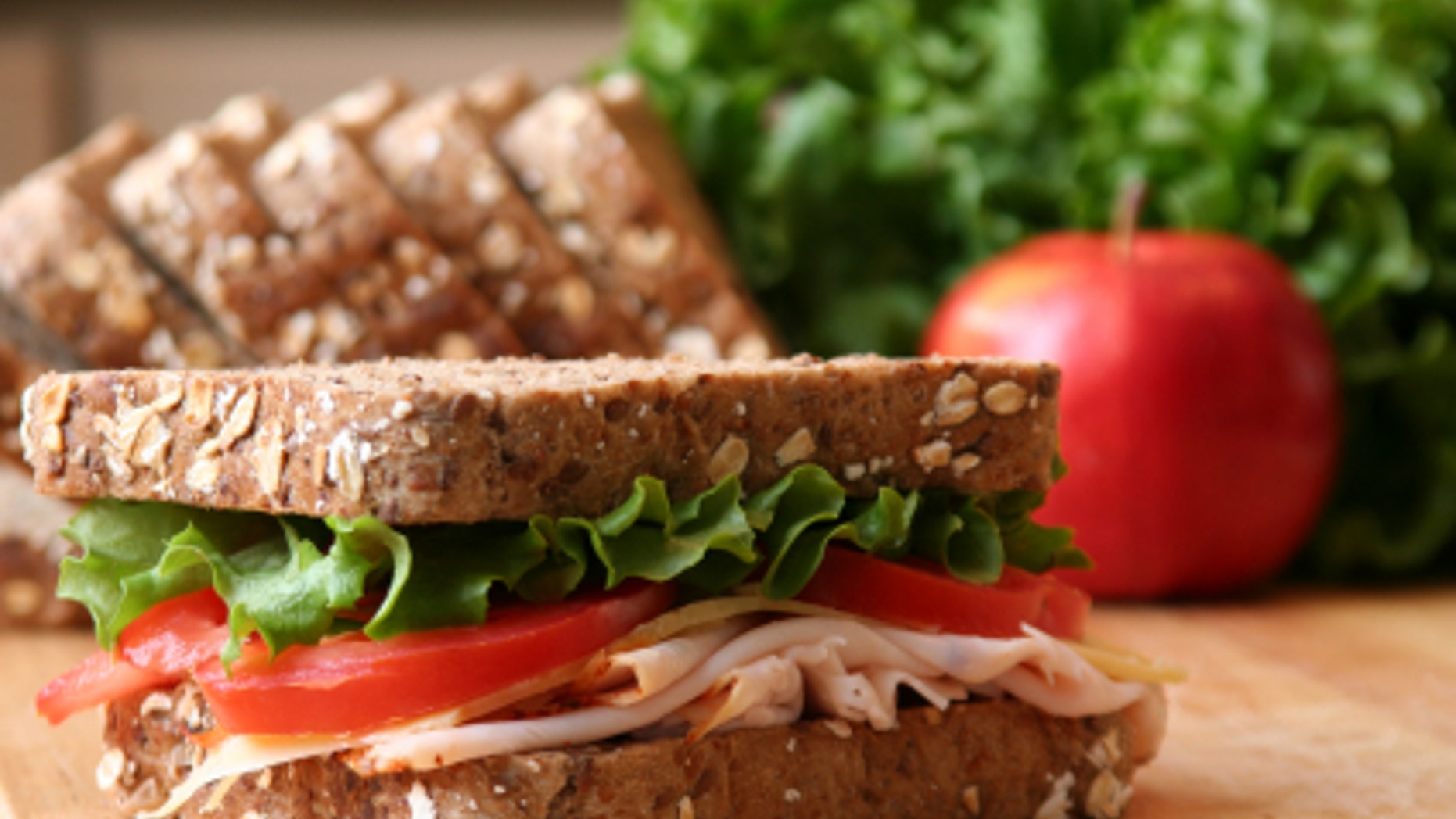 Healthy sandwhich made with whole grain bread, lettuce, tomato, cheese, and roasted chicken slices.