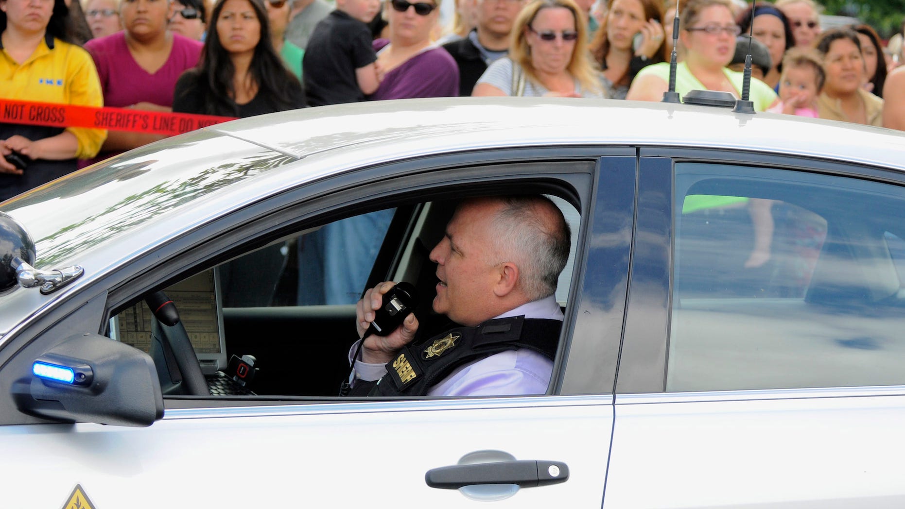 In this June 10, 2014, file photo, a sheriff's deputy talks on his radio as parents wait to be reunited with their children at a shopping center parking lot in Wood Village, Ore., after a shooting at Reynolds High School in Troutdale, Ore.