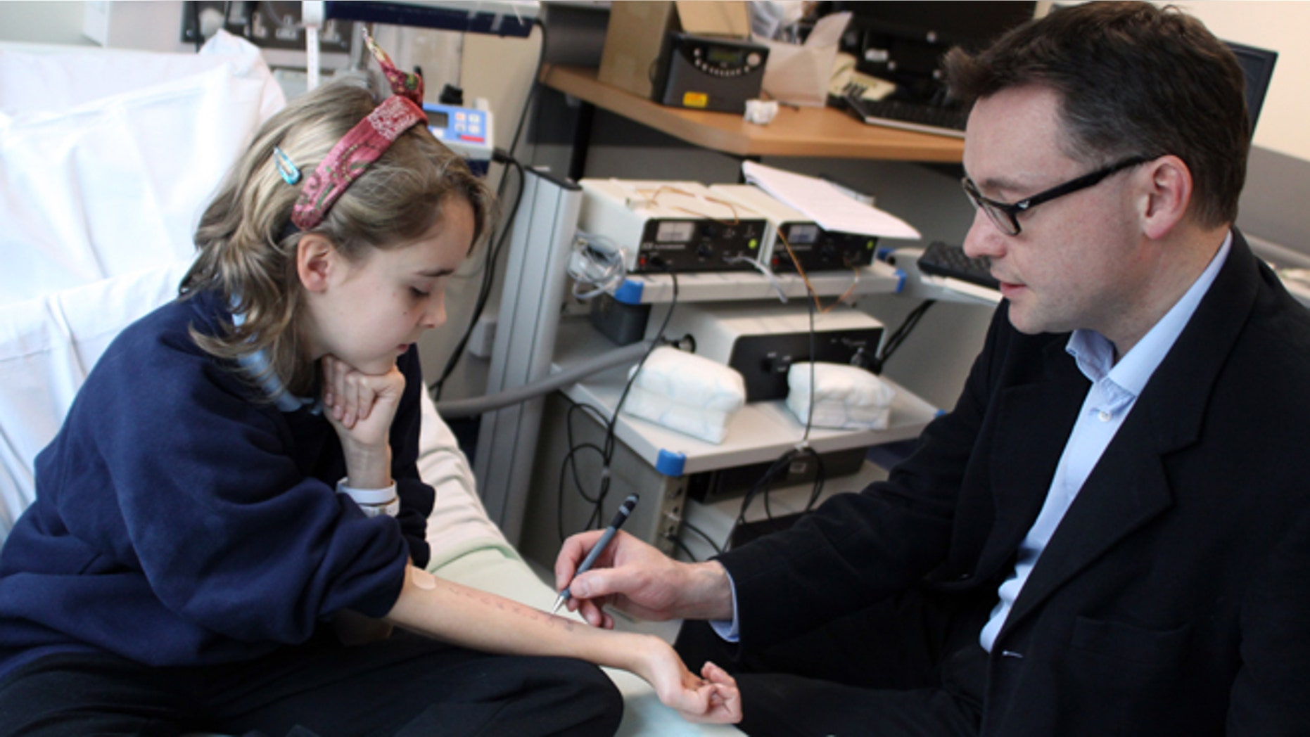 In this undated photo provided by Cambridge University Hospitals NHS Foundation Trust, Dr. Andrew Clark of Cambridge University, right, performs a skin prick test, which is used to diagnose food allergies, on Lena Barden, 12, during clinical trials at Addenbrooke's Hospital Clinical Research Facility, Cambridge, England. An experimental therapy in Britain that fed children with peanut allergies small amounts of peanut flour has helped more than 80 percent of them eat a handful of the previously worrisome nuts safely. Though experts say the results are encouraging, they warn it isnât something people should try at home. (AP Photo/Cambridge University Hospitals NHS Foundation Trust)