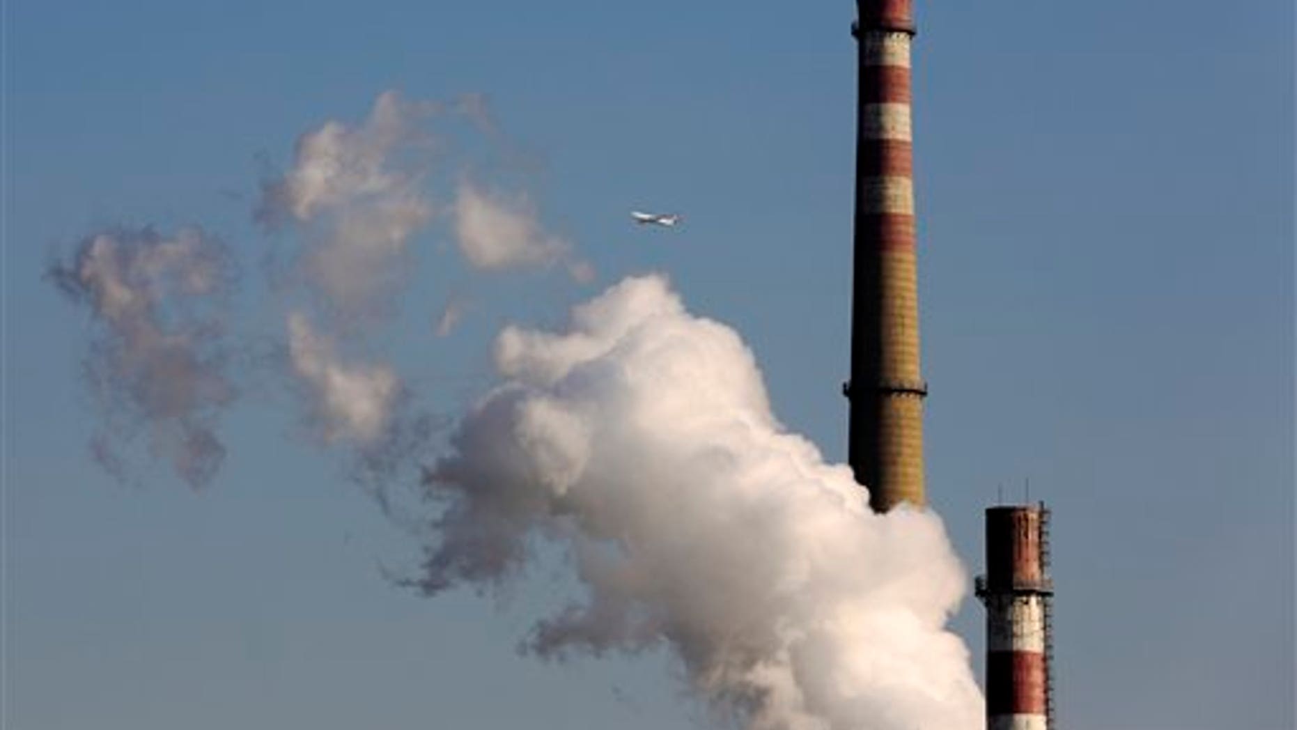 In this Nov. 13, 2014, photo, a passenger airliner flies past a coal-fired power plant in Beijing, China. U.N. climate talks are plodding ahead toward a worldwide deal to fight global warming. (AP Photo/Andy Wong, File)