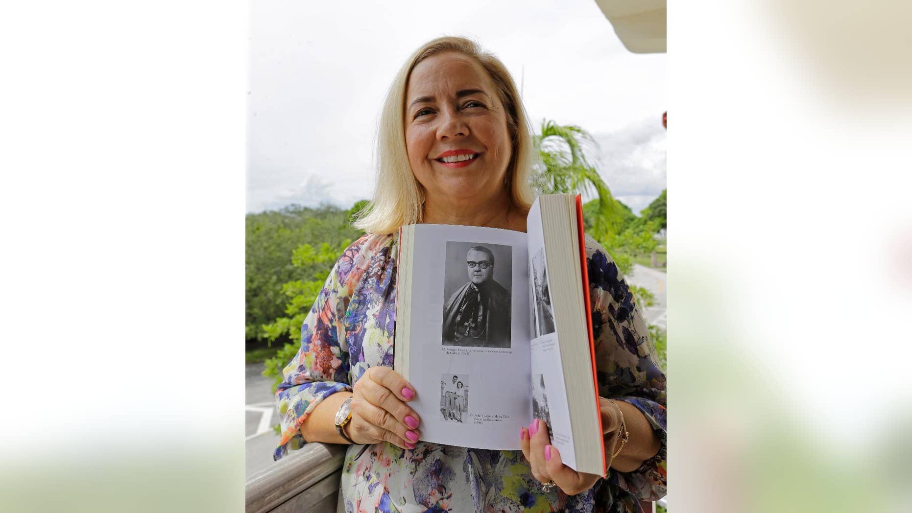 In this Sept. 10, 2015 photo, Frances Serantes Gomez poses with a photo of her great uncle, Archbishop Enrique Perez Serantes, at her home in Coral Gables, Florida. Serantes Gomez's great uncle is the former archbishop of Santiago, Cuba who saved Fidel Castro’s life. After Castro seized power, Serantes’ support turned to opposition and the prelate’s family fled. Frances is among several hundred Cuban-Americans expected to make a pilgrimage to Cuba for Pope Francis’ visit, and among thousands who are trying to finally put five decades of bitterness behind them. (AP Photo/Alan Diaz)