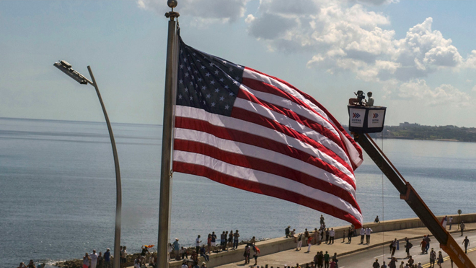 In this photo taken through a window, Cuban videographers film the U.S. flag from a crane after it was raised at the U.S. Embassy in Havana, Friday, Aug. 14, 2015. The Stars and Stripes rose over the newly reopened U.S. Embassy after a half-century of broken diplomatic relations. (AP Photo/Ramon Espinosa)