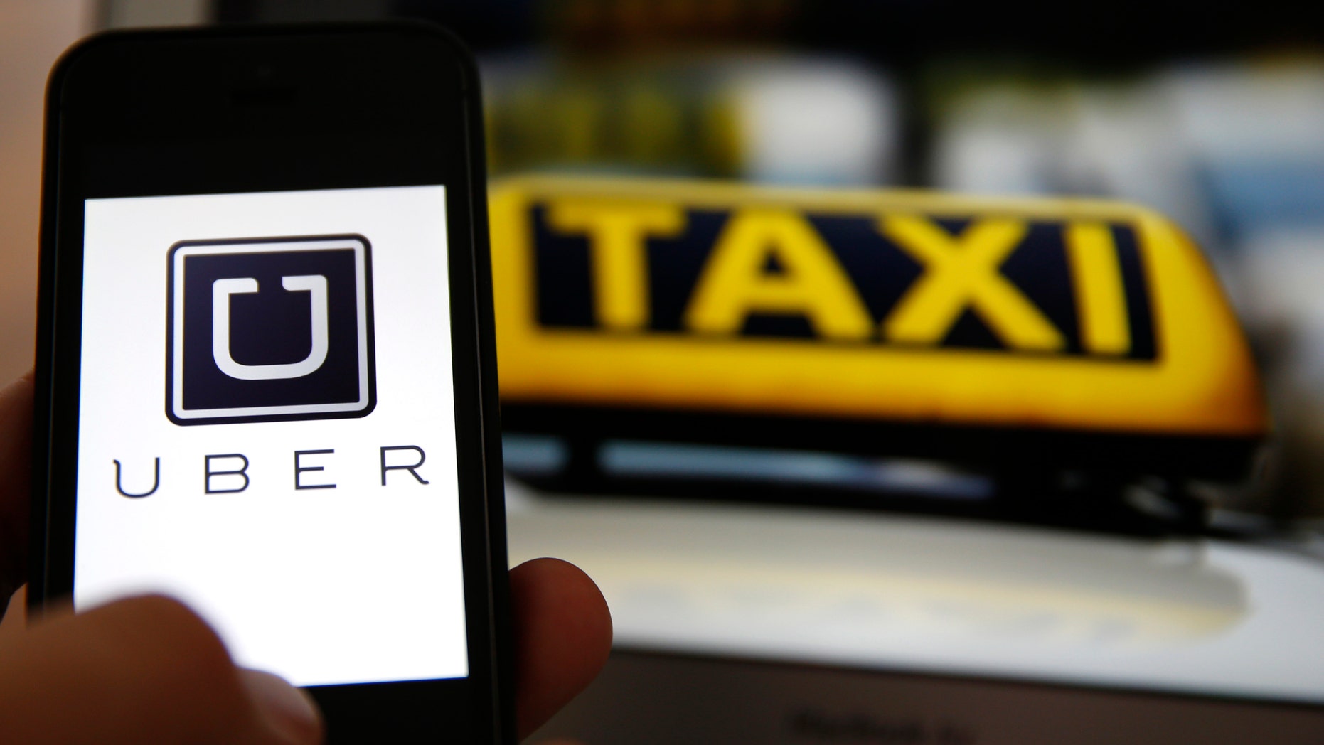 An illustration picture shows the logo of car-sharing service app Uber on a smartphone next to the picture of an official German taxi sign in Frankfurt, Germany.