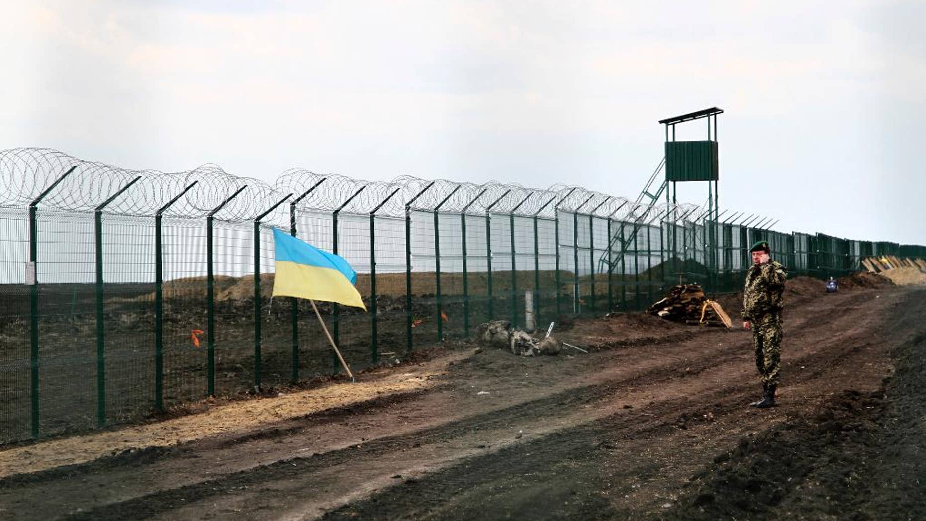 In this photo taken on Saturday, April 18, 2015, a Ukrainian border guard officer speaks on a phone near a national flag attached to the fence on the Ukrainian-Russian border near Hoptivka, Kharkiv region, eastern Ukraine. The flimsy, razor wire-topped fences popping up along bare expanses of Ukraine’s eastern frontier are the first line of defense against a much-feared Russian invasion. (AP Photo/Inna Varenytsia)