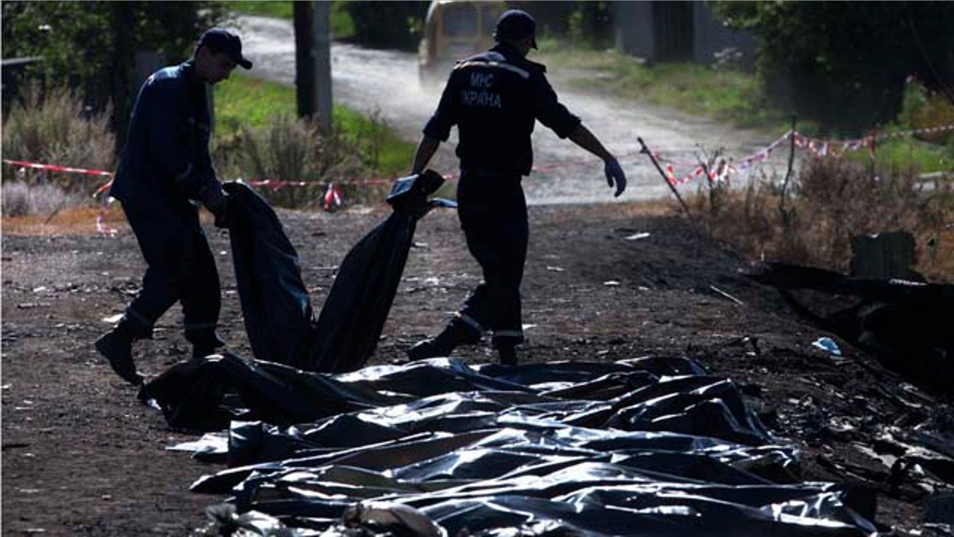 July 21, 2014: Ukrainian Emergency workers carry a victim's body in a plastic bag as other bodies are laid on the ground nearby at the crash site of Malaysia Airlines Flight 17 near the village of Hrabove. (AP Photo/Dmitry Lovetsky)
