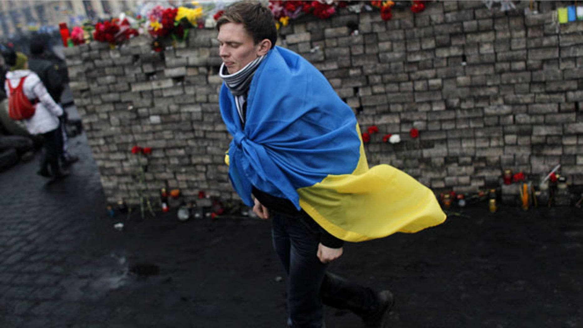 February 23, 2014: A youth draped in Ukraine's flag passes by a memorial to protesters killed in clashes with the police at Independence Square in Kiev, Ukraine. (AP Photo/ Marko Drobnjakovic)