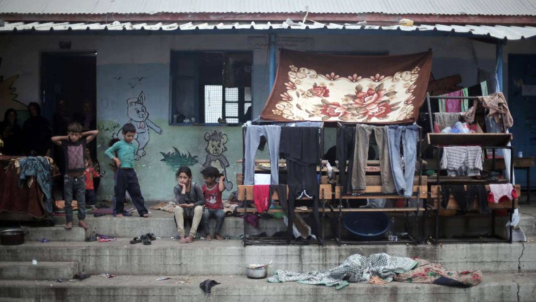 FILE - In a July 28, 2014 file photo, Palestinian children sit next to hanged clothes, on the First day of Eid al-Fitr in a United Nations school where dozens of families have sought refuge after fleeing their homes in fear of Israeli airstrikes, in the Jabaliya refugee camp, northern Gaza Strip. A U.N. inquiry has found that at least 44 Palestinians were killed and at least 227 injured by "Israeli actions" while sheltering at U.N. locations during last year's Gaza war. Secretary Ban Ki-moon said Monday, April 27, 2015, he deplores the deaths and calls U.N. locations "inviolable."(AP Photo/Khalil Hamra, File)