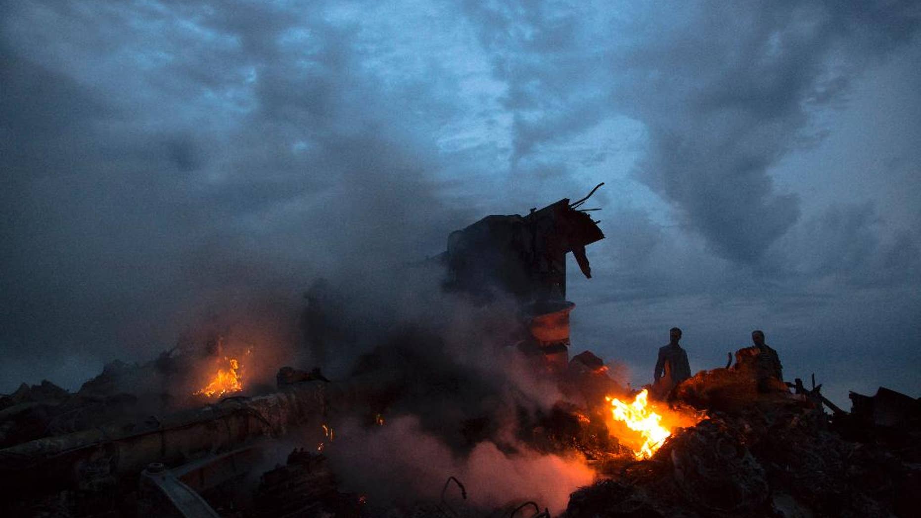 File - This July 17, 2014, file photo shows people walking amongst burning debris at the crash site of Malaysia Airlines Flight 17 near the village of Hrabove, eastern Ukraine. Ukraine said the passenger plane was shot down as it flew over the country, killing all 298 people on board. A series of unanswered questions about the downing the flight shows the limits of U.S. intelligence-gathering even when it is intensely focused, as it has been in Ukraine since Russia seized Crimea in March. (AP Photo/Dmitry Lovetsky, File)