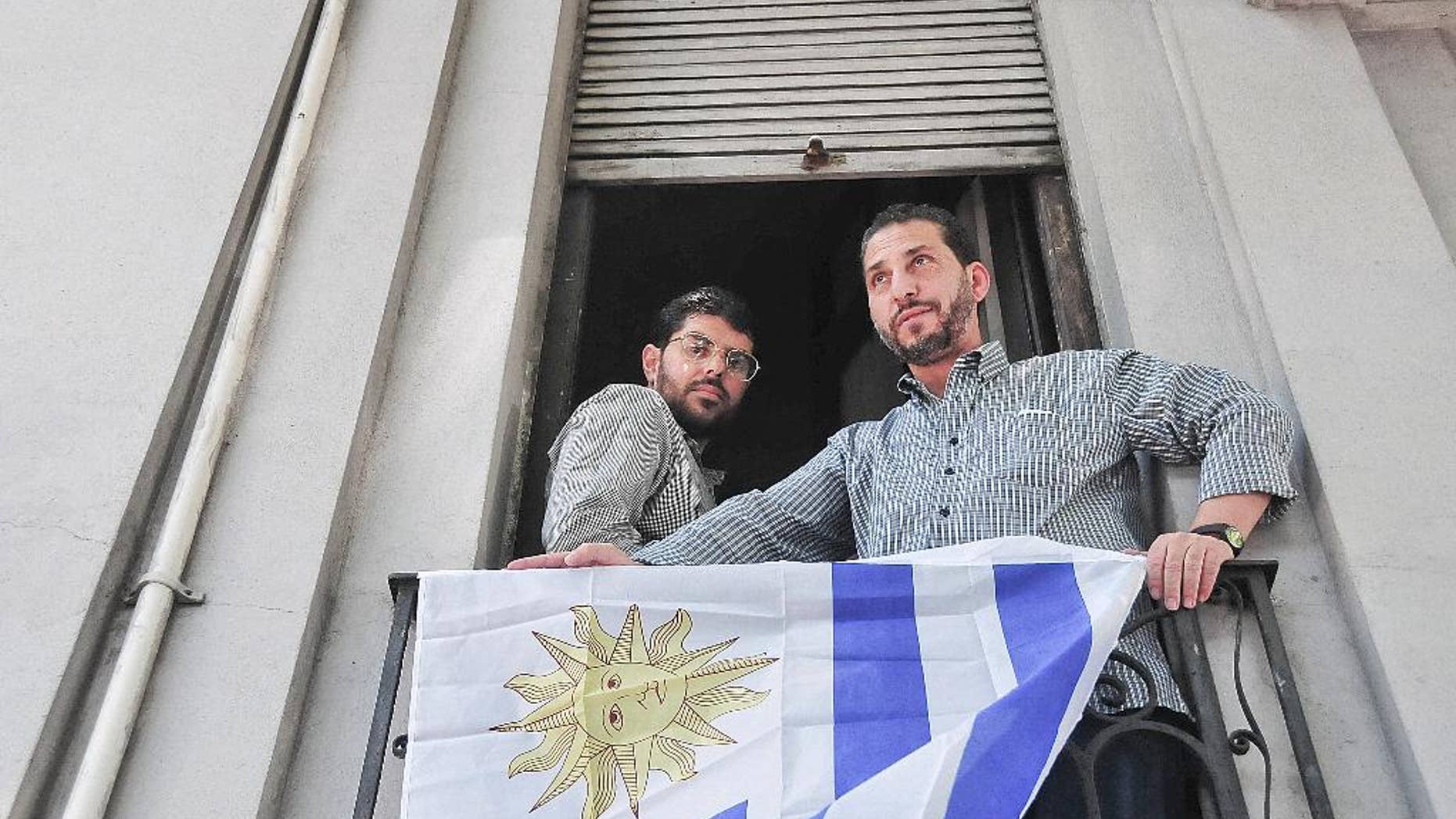 FILE - In this Dec. 11, 2014 file photo, Omar Abdelahdi Faraj, of Syria, left, and Adel bin Muhammad El Ouerghi, of Tunisia, look out at the press from their shared home's balcony decorated with Uruguay's flag in Montevideo, Uruguay. The two former Guantanamo Bay detainees who resettled in Uruguay are planning to tie the knot with women from the South American country. Imam Samir Selim said on Thursday, May 28, 2015 that he would officiate the ceremony. (Ines Guimaraens, Diario El Observador via AP, File) URUGUAY OUT - NOT FOR USE ON URUGUAY WEBSITES OR PUBLICATIONS - NO PUBLICAR EN URUGUAY - NO USAR EN PAGINAS WEBS O EN PAPEL EN URUGUAY