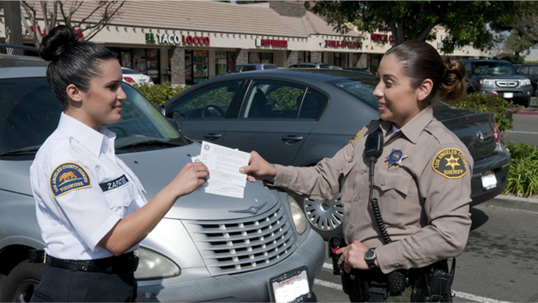 A deputy hands crime prevention tips to a Los Angeles County Sheriff's Department civilian volunteer, who are now allowed to issue parking violations to Malibu residents. (Courtesy: LASCD)