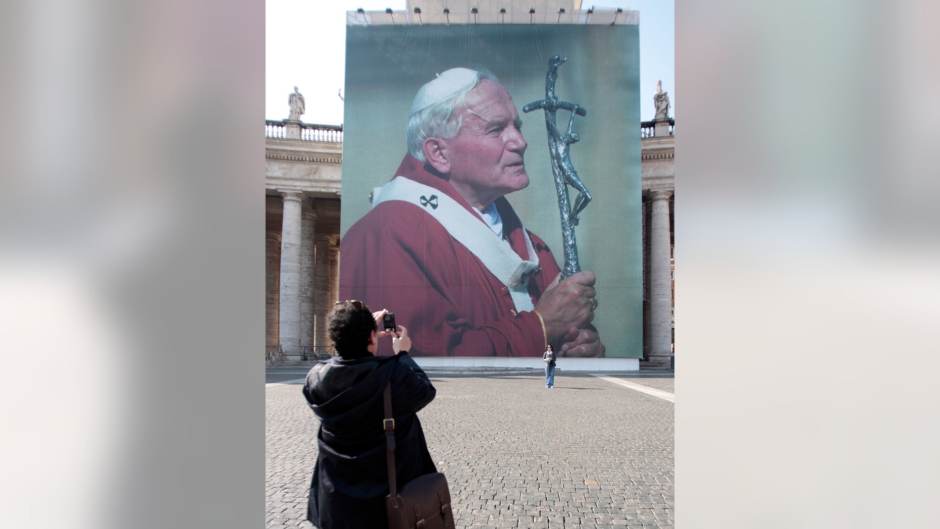 Faithful take a suovenir picture in front of a giant poster of late Pope John Paul II, in St. Peter's square, at the Vatican, April 28, 2011, days before John Paul's May 1 beatification. A prayer vigil on the Circus Maximus, an all-night prayer session in downtown Rome churches and the beatification Mass celebrated by Pope Benedict XVI top the agenda for the three-day event.