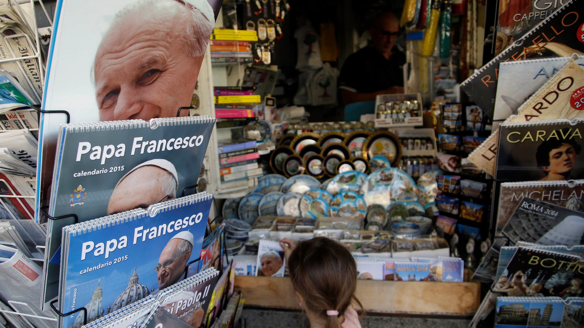 A child picks up a souvenir at a newspaper kiosk near the Vatican, Friday, April 25, 2014. Hundred thousands of pilgrims and faithful are expected to reach Rome to attend the scheduled April 27 ceremony at the Vatican in which Pope Francis will elevate in a solemn ceremony John XXIII and John Paul II to sainthood. (AP Photo/Gregorio Borgia)