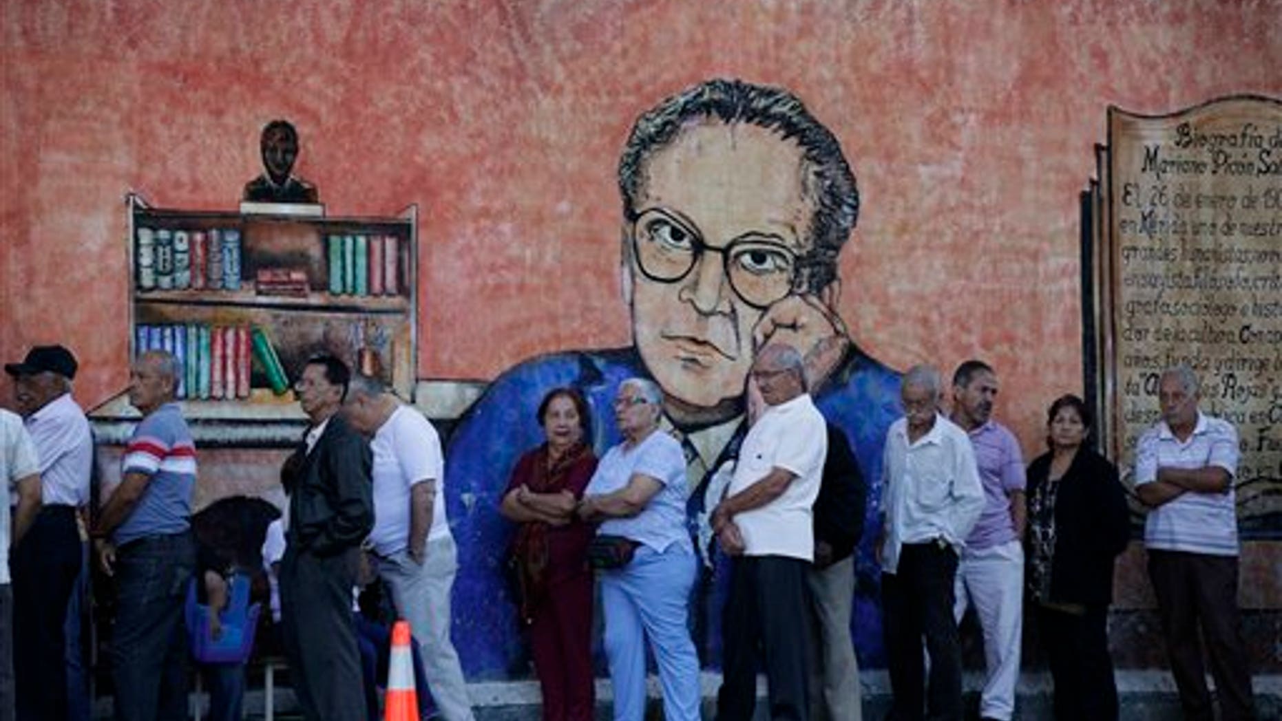 Residents in front of a wall with a painting depicting Venezuelan writer and diplomat Mariano Picon as they wait in line to enter a polling station to vote during municipal elections in Caracas, Venezuela, Sunday, Dec. 8, 2013. Venezuelans head to the polls to elect mayors and city councilors at a moment when the country's economic troubles have deepened, with inflation touching a two-decade high of 54 percent, and shortages of everything from toilet paper to milk spreading while the black market value of the currency plunges. (AP Photo/Ariana Cubillos)