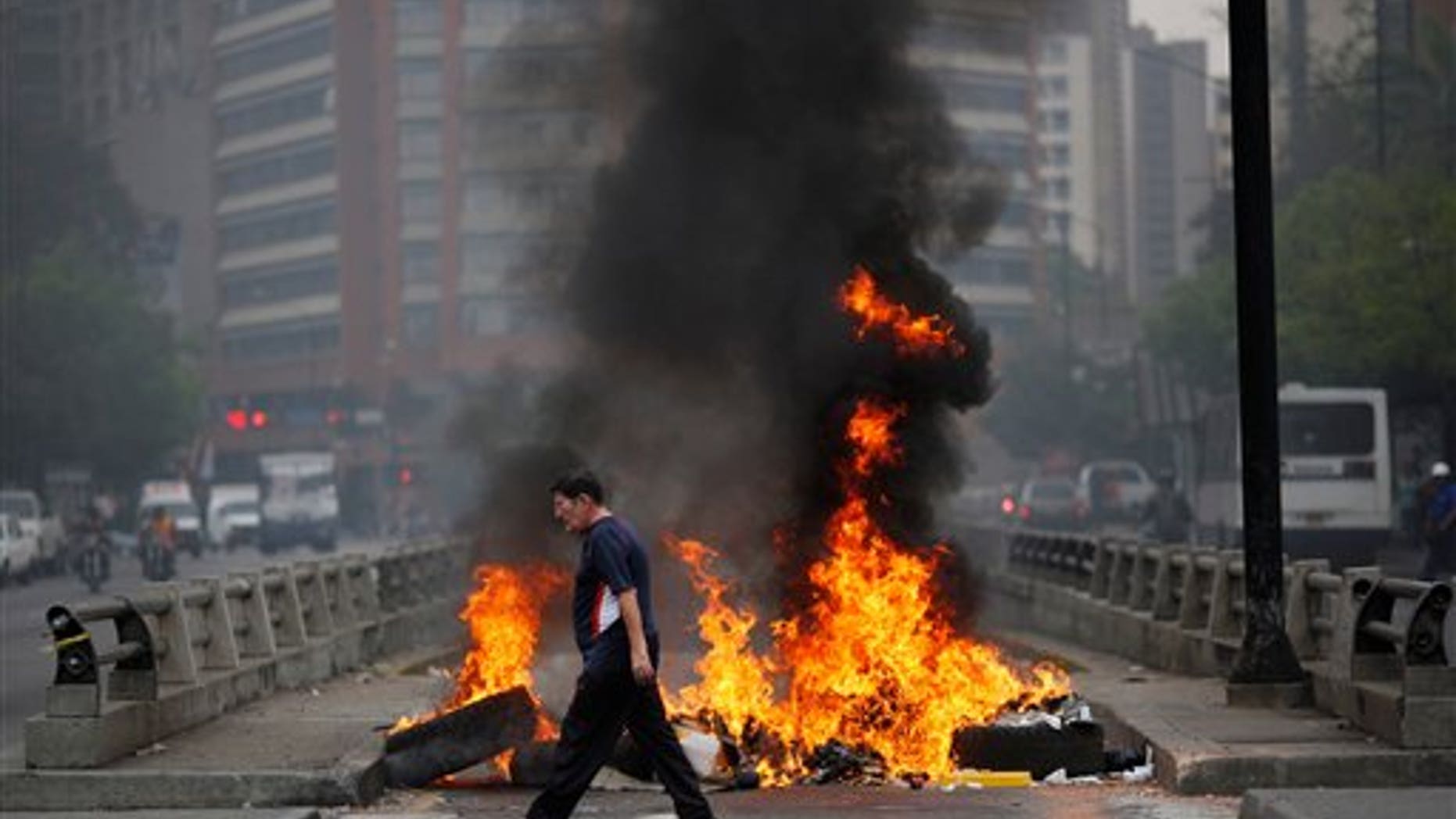 A pedestrian walks in front of a burning barricade blocking the highway in Chacao, Caracas, Venezuela, Monday, Feb. 24, 2014. Traffic has come to a halt in parts of the Venezuelan capital because of barricades set up by opposition protesters across major thoroughfares. The protests are part of a wave of anti-government demonstrations that have swept Venezuela since Feb. 12 and have resulted in at least 10 deaths. The protests in the capital Monday were peaceful. Police and National Guard troops stood by but did not act to remove the barricades despite the effect on the morning commute. (AP Photo/Rodrigo Abd)