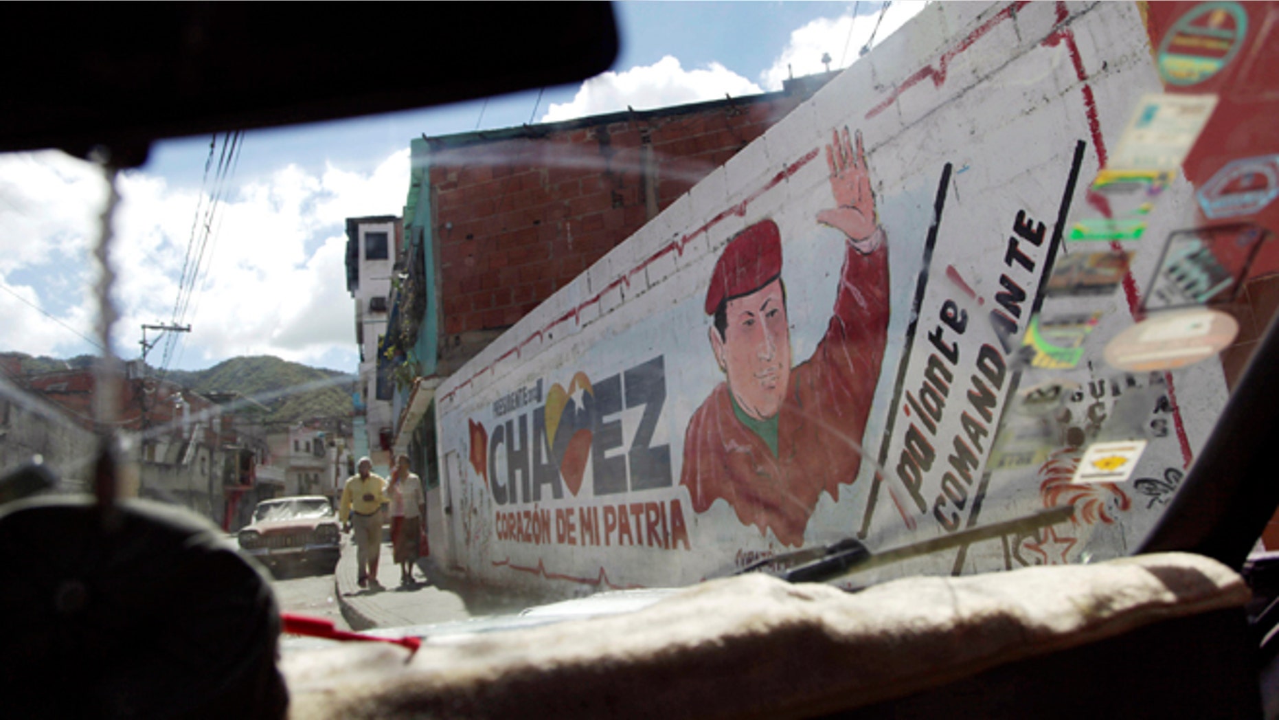 The windshield of a car frames a mural of Venezuela's President Hugo Chavez in Caracas, Venezuela, Wednesday, Jan. 2, 2013. Venezuela's vice president is returning home Wednesday from a visit with Chavez in Cuba and says the ailing president's condition remains "delicate" three weeks after his cancer surgery. (AP Photo/Ariana Cubillos)