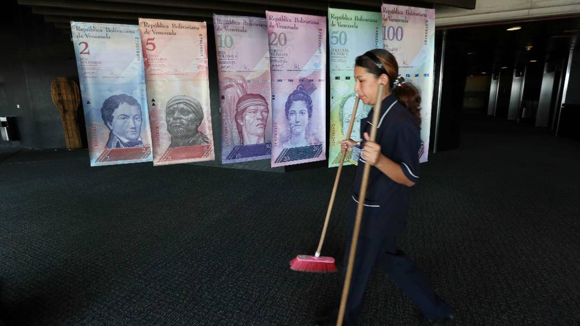 FILE - In this Feb. 10, 2015 file photo, a cleaning woman walks by replicas of Venezuela's currency bills, hung in a hallway at the Central bank office building in Caracas, Venezuela. The South American country debuted a new exchange system last week aimed at easing the country's economic crisis, and on Thursday, Feb. 19, 2015, Venezuelans got their first crack at trading local cash for paper dollars at banks and money exchangers. (AP Photo/Ariana Cubillos, File)