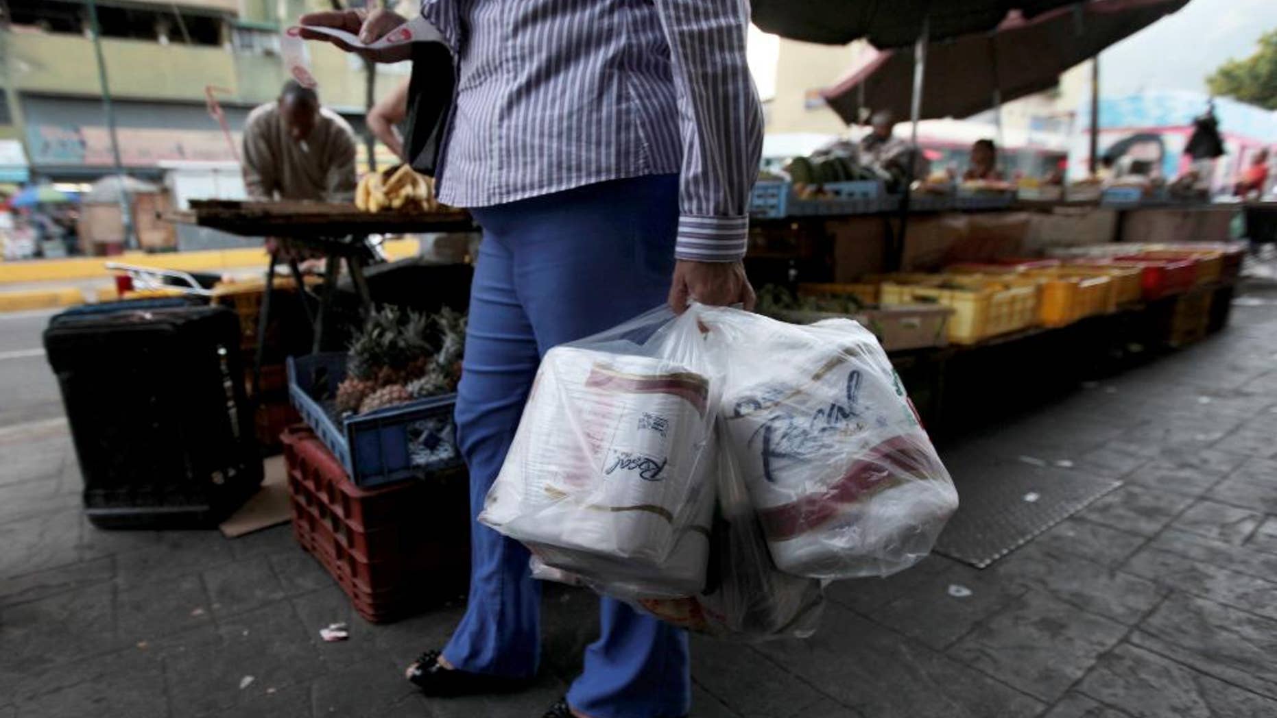 FILE- In this May 15, 2013 file photo, a woman who just bought toilet paper at a grocery store reads her receipt as she leaves the private store in Caracas, Venezuela. On Wednesday Sept. 10, 2014, Venezuela's President Nicolas Maduro reassured foreign creditors that his government will make good on a $4.5 billion foreign debt payment due next month. (AP Photo/Fernando Llano, File)