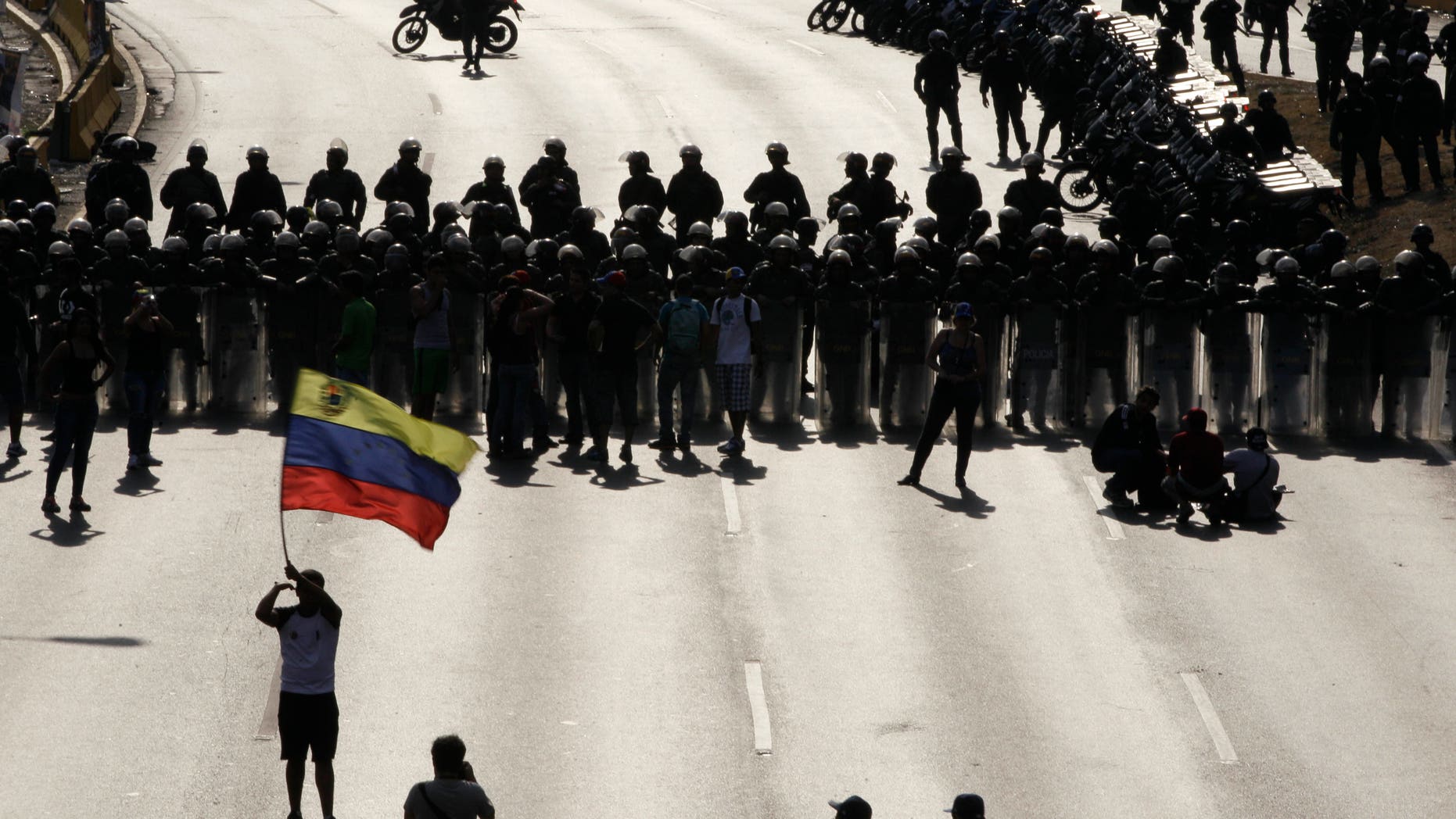 An opposition supporter waving a Venezuelan flag stands before riot police blocking a highway in the Altamira neighborhood of Caracas, Venezuela, Monday, April 15, 2013. National Guard troops fired tear gas and plastic bullets to disperse students protesting the official results in Venezuela's disputed presidential election. Opposition candidate Henrique Capriles has challenged his narrow loss to Nicolas Maduro and is demanding a recount. (AP Photo/Fernando Llano)