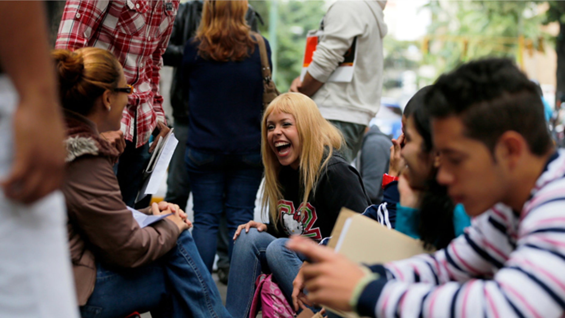 In this Jan. 28, 2014 photo, Daniela Rodriguez laughs with friends as she waits outside Ireland's consulate in Caracas, Venezuela. Venezuela's best and brightest are abandoning their homeland in droves. "I'll blindly go anywhere," said Rodriguez, who has been unable to find work as a journalist since graduating college in 2010, so instead works as a sales clerk at a clothing store. (AP Photo/Fernando Llano)