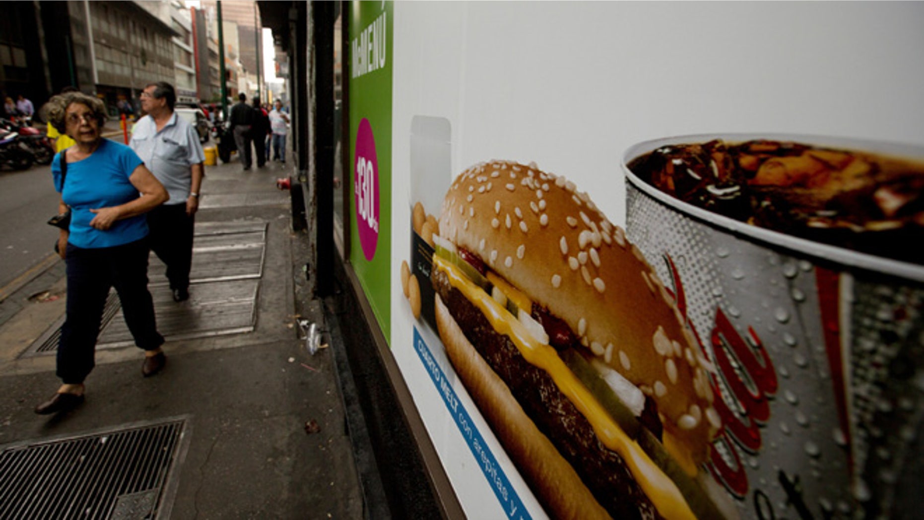 FILE - In this Jan. 6, 2015 file photo, a customer glances at a McDonalds' banner menu showing a burger accompanied by arepas or corn cakes, instead of fries, in Caracas, Venezuela. Fast food lovers in shortage-plagued Venezuela are rejoicing they can once again buy greasy French fries at McDonaldâs franchises after the side dish went missing last winter. Sonia Ruseler, an Argentina-based spokeswoman for Arcos Dorados, which runs McDonald's restaurants in Latin America, says the company was able to bring the fries back by sourcing potatoes locally. (AP Photo/Fernando Llano, File)