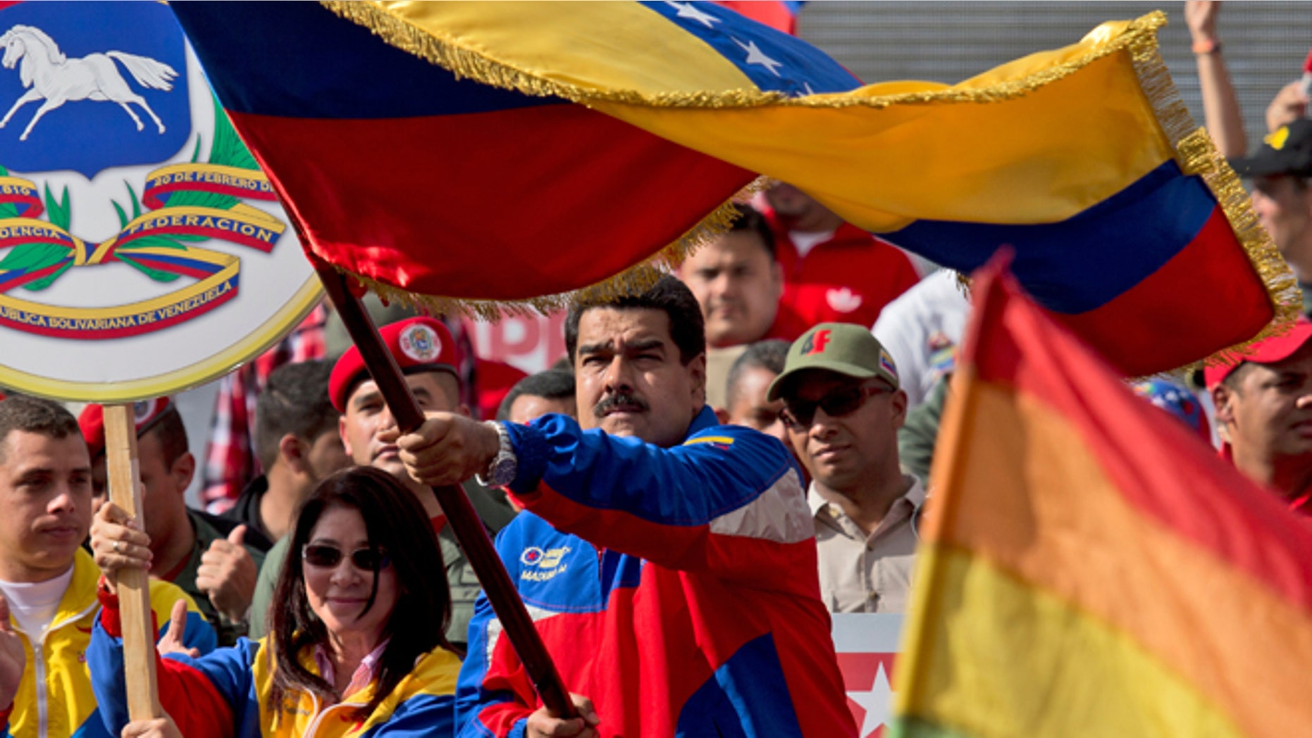 Venezuela's President Nicolas Maduro, center, waves a national flag during a rally in Caracas, Venezuela, Saturday, Feb. 28, 2015. Venezuelans took to the streets of Caracas in dueling demonstrations on Saturday, with one group calling attention to a crackdown on opponents of the government and another showing support for the embattled socialist administration. At left is Venezuela's first lady Cilia Flores. (AP Photo/Fernando Llano)