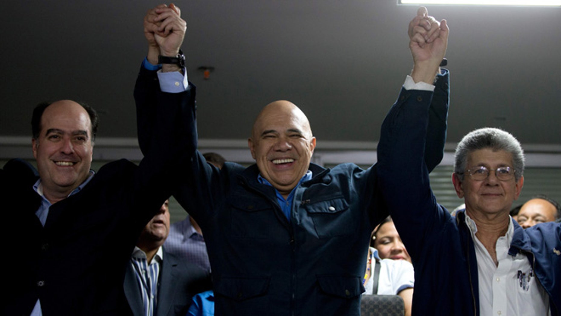 The General Secretary of Opposition coalition Jesus Torrealba, center, rise the arms of Venezuela National Assembly President candidates Julio Borges, left, and Henry Ramos Allup, right, in Caracas, Venezuela, Sunday, Jan. 3, 2016. Newly-elected opposition lawmakers voted in Ramos as National Assembly president Sunday. (AP Photo/Fernando Llano)