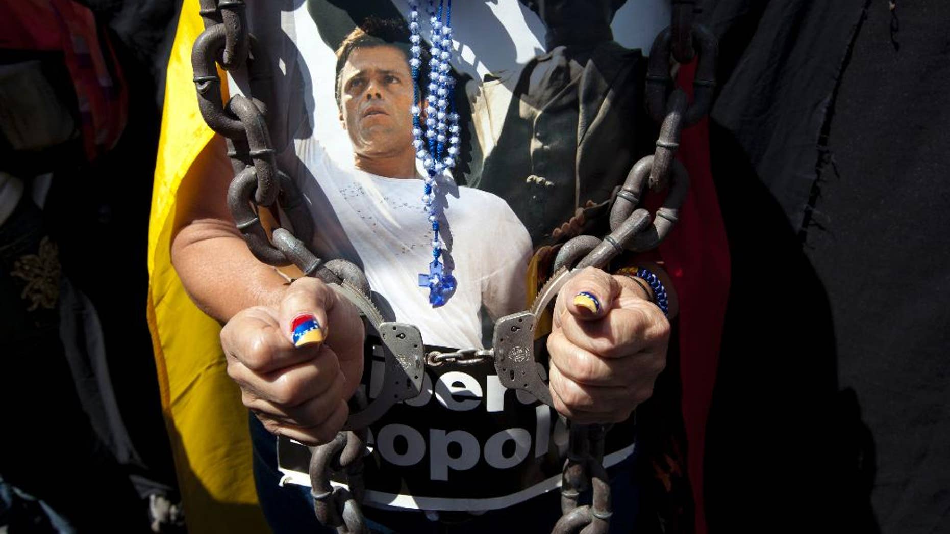FILE - In this Feb. 18, 2015 file photo, a woman wearing handcuffs, chains and a rosary holds a poster of jailed opposition leader Leopoldo Lopez at an event marking the one year anniversary of his arrest and imprisonment in Caracas, Venezuela. Prosecutor Franklin Nieves, who reportedly is now seeking asylum in the United States, said in a video posted Monday, Oct. 26, 2015 on the Venezuelan news website La Patilla that superiors in the prosecutor's office had given him orders to have Lopez arrested days before the Caracas protest - and the alleged crime - took place. Lopez was convicted in September 2015 of inciting violence during a 2014 anti-government protest in Caracas and received the maximum sentence, about 14 years. (AP Photo/Ariana Cubillos, File)