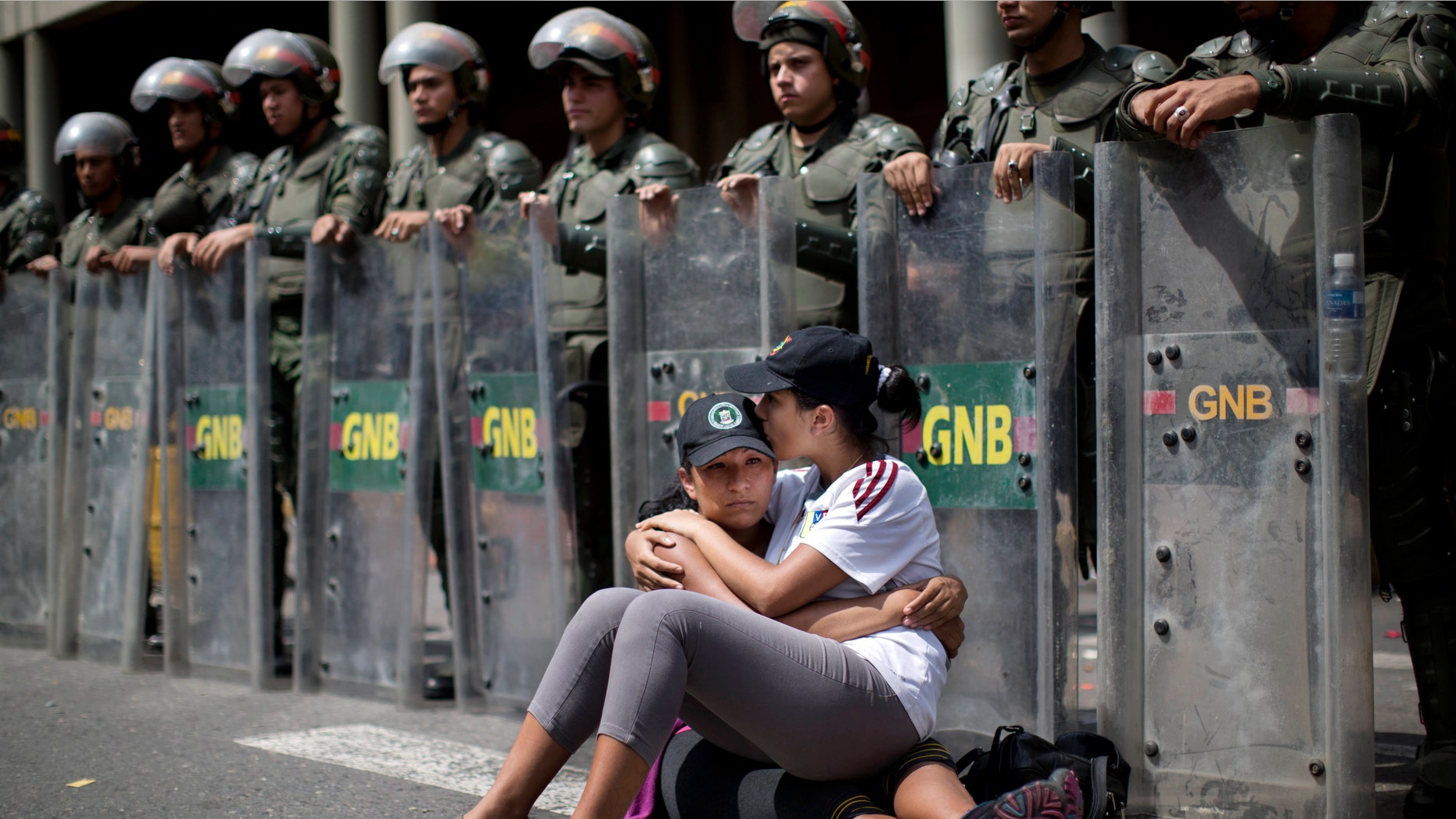 Women embrace as they sit in front of a line of National Bolivarian Guard outside the Palace of Justice court in Caracas, Venezuela, Wednesday, Feb. 19, 2014. Following a dramatic surrender and a night in jail, Venezuelan opposition leader Leopoldo Lopez was due in court Wednesday to learn what charges he may face for allegedly provoking violence during protests against the socialist government in the divided nation. (AP Photo/Rodrigo Abd)