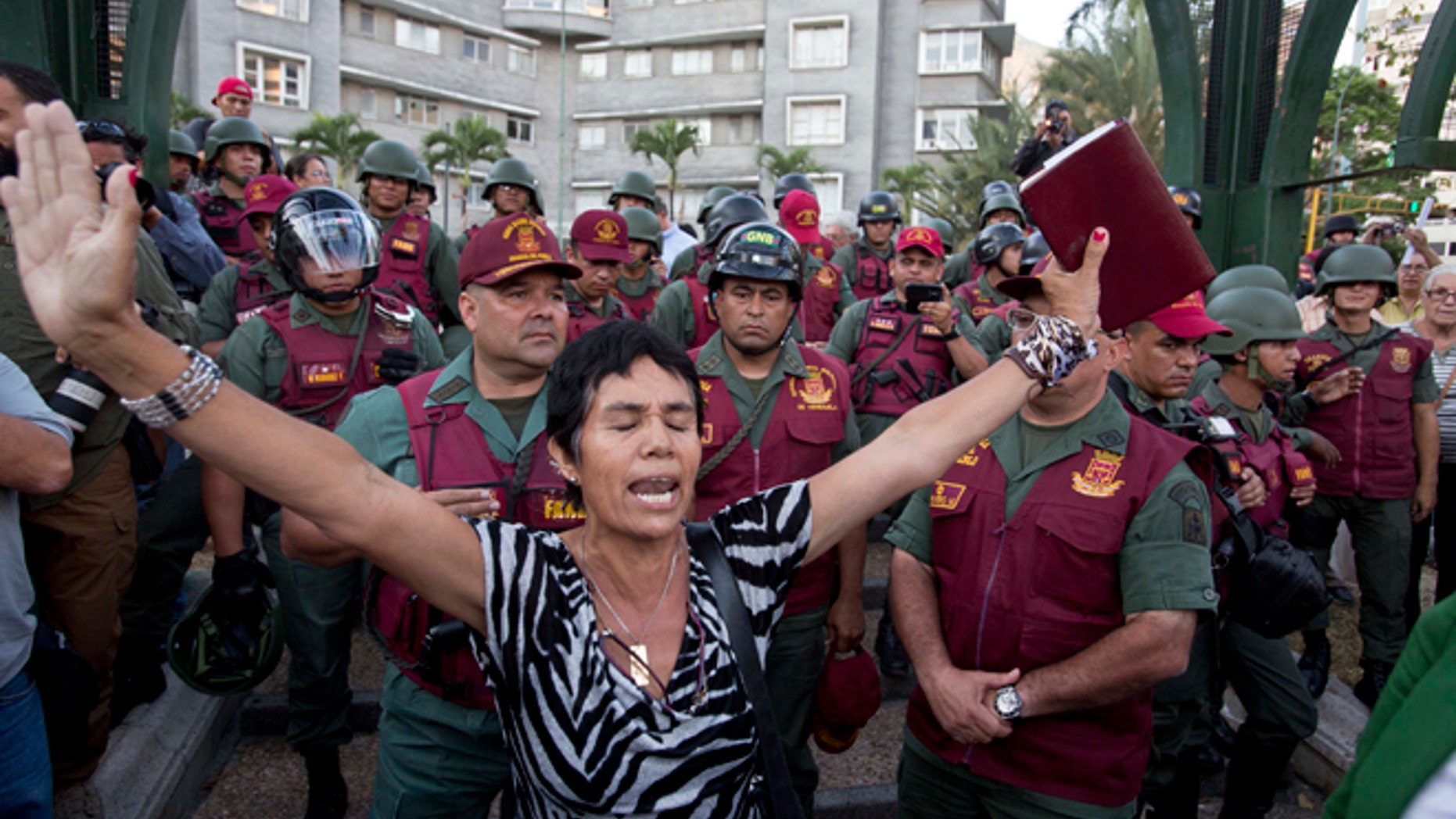 A woman prays with a bible in her hand, in front of Bolivarian National Guard officers during an anti-government protest in Plaza Altamira, Caracas, Venezuela, Tuesday, March 18, 2014. Protesters blocked the streets only when traffic lights turned red under the watchful gaze of the National Guard. Security forces have taken control of the plaza that has been at the heart of anti-government protests that have shaken Venezuela for a month. (AP Photo/Esteban Felix)