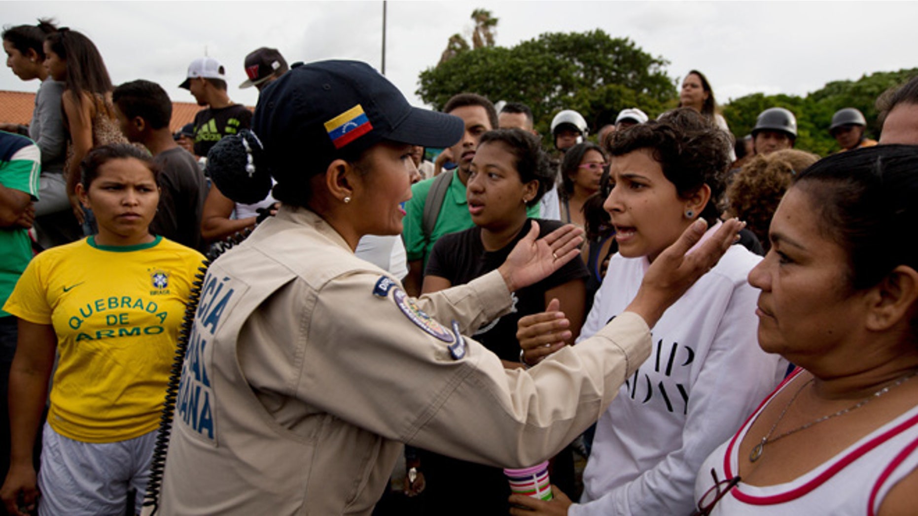 A police officer talks to an angry crowd during a protest for food at the Catia neighborhood in Caracas, Venezuela, Tuesday, June 14, 2016. Tensions rose after customers waited in line for hours and their frustration turned into a street protest. (AP Photo/Fernando Llano)